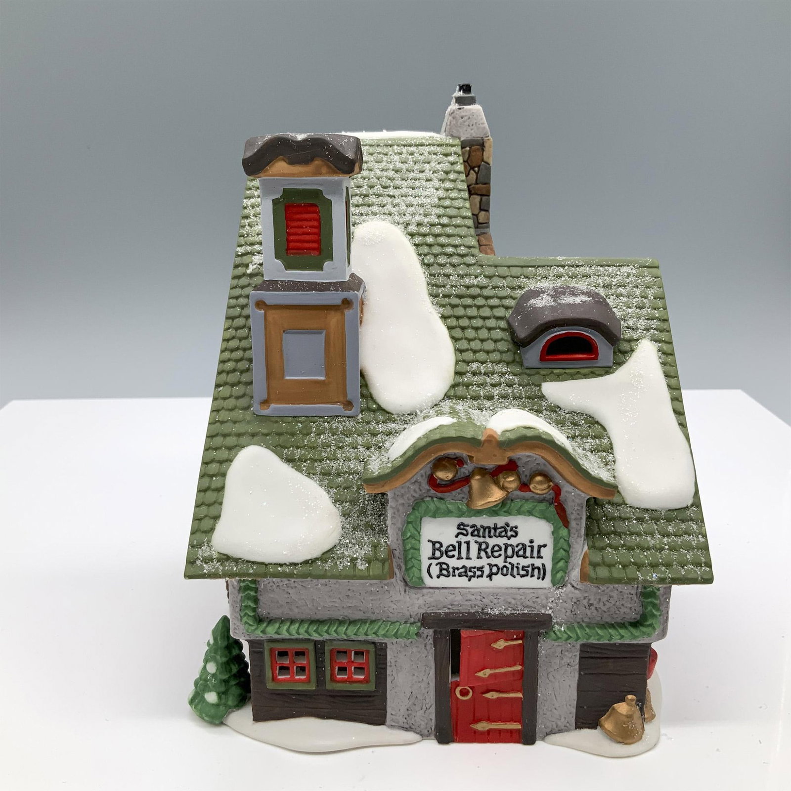 Department 56 North Pole Series Figurine: Hand painted porcelain house titled Santa's Bell Repair from the Heritage Village Collection's North Pole Series. This festive shop features a glittering snow covered green roof, a half open red door,