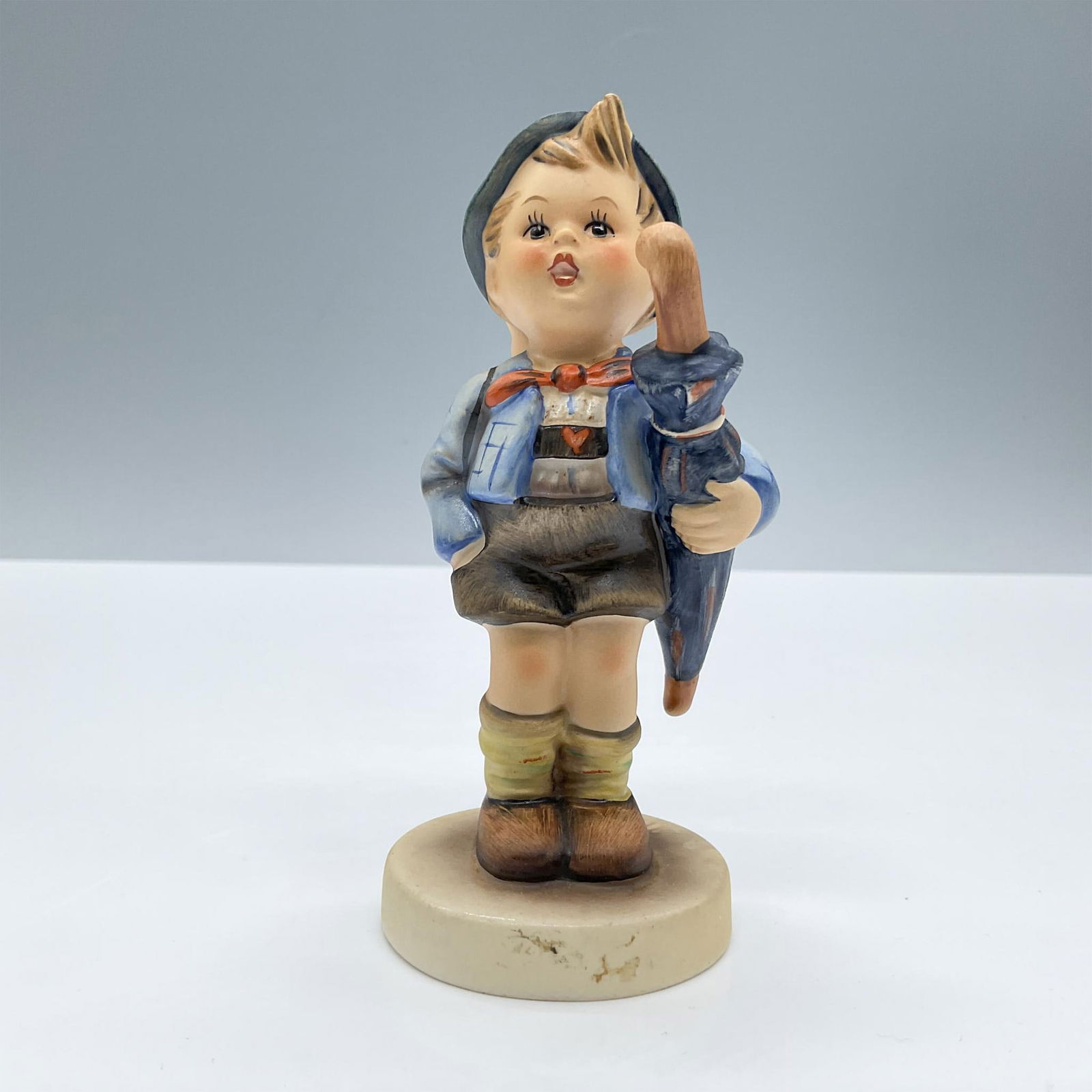 Goebel Hummel Figurine, Home From Market: Features an adorable child carrying a little pig and a blue umbrella. Goebel Hummel backstamp. Issued: 20th century Dimensions: 2.5''L x 2''W x 4.75''H Manufacturer: Goebel Hummel Country of Origin: G