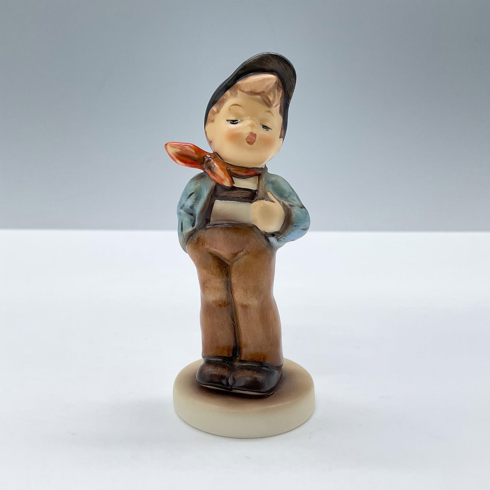 Goebel Hummel Figurine, Lucky Fellow 560: Presenting an adorable boy un blue and brown clothes with red scarf. 'M. I. Hummel' inscribed on base. 1992/1993 exclusive edition for Hummel Club members. Goebel backstamp. This item has its original