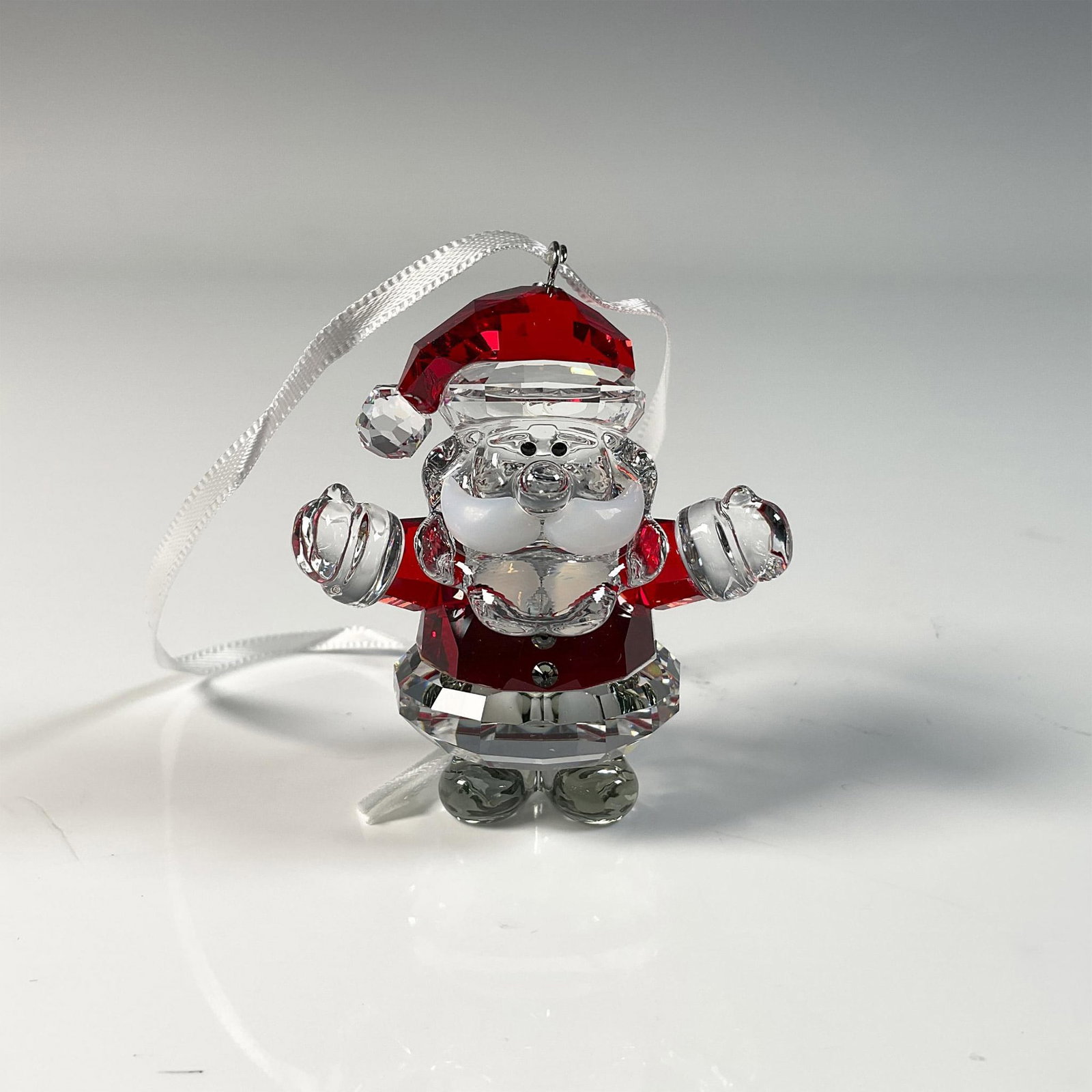 Swarovski Christmas Ornament, Santa Claus: Delightful Christmas tree ornament featuring Santa Claus, crafted from clear crystal with red accents. Swarovski swan mark. This item includes original box: 3"L x 3"W x 1.5"H. 5286070. Artist: Edith M