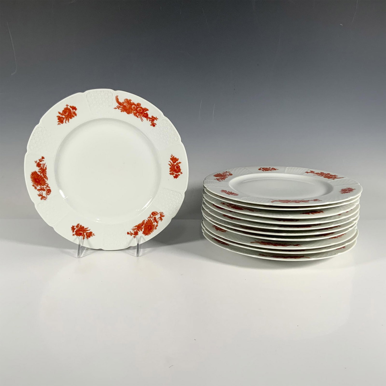 11pc GDA Limoges Floral Plates: A captivating set of white plates, beautifully decorated with a rim that alternates between vibrant red floral designs and intricate low relief wicker patterns. Marked GDA. Marked Limoges France. Dime