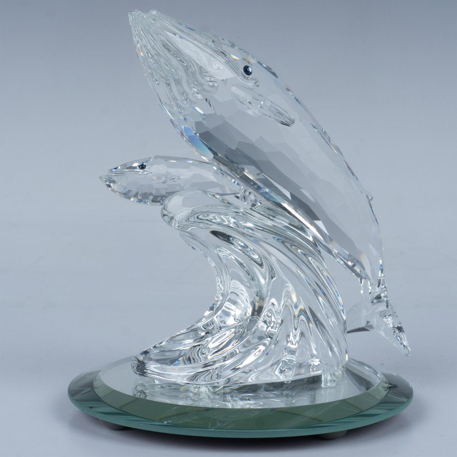 2pc Swarovski Crystal Figurine and Base, Care for Me 164614: A mother and baby whale swim side by side over a wave, radiating love, both adorned with striking blue crystal eyes. Includes circular mirror base. Swarovski backstamp. This item has its original box.