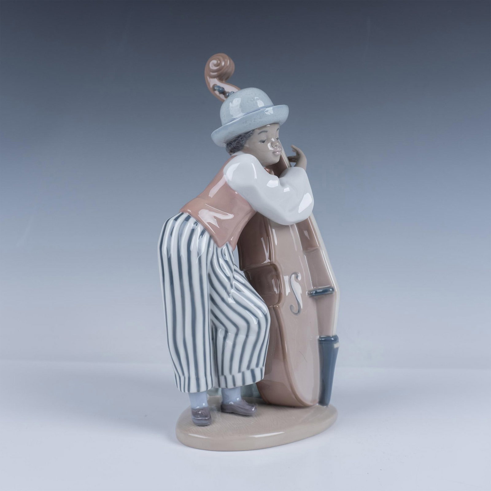 Lladro Porcelain Figurine, Jazz Bass: Glossy figure of a young man leaning across his instrument. Lladro backstamp. 1005834. This item has its original box 12.75"L x 7.5"W x 6"H. This item has its original box. Artist: Rafael Lozano Issue