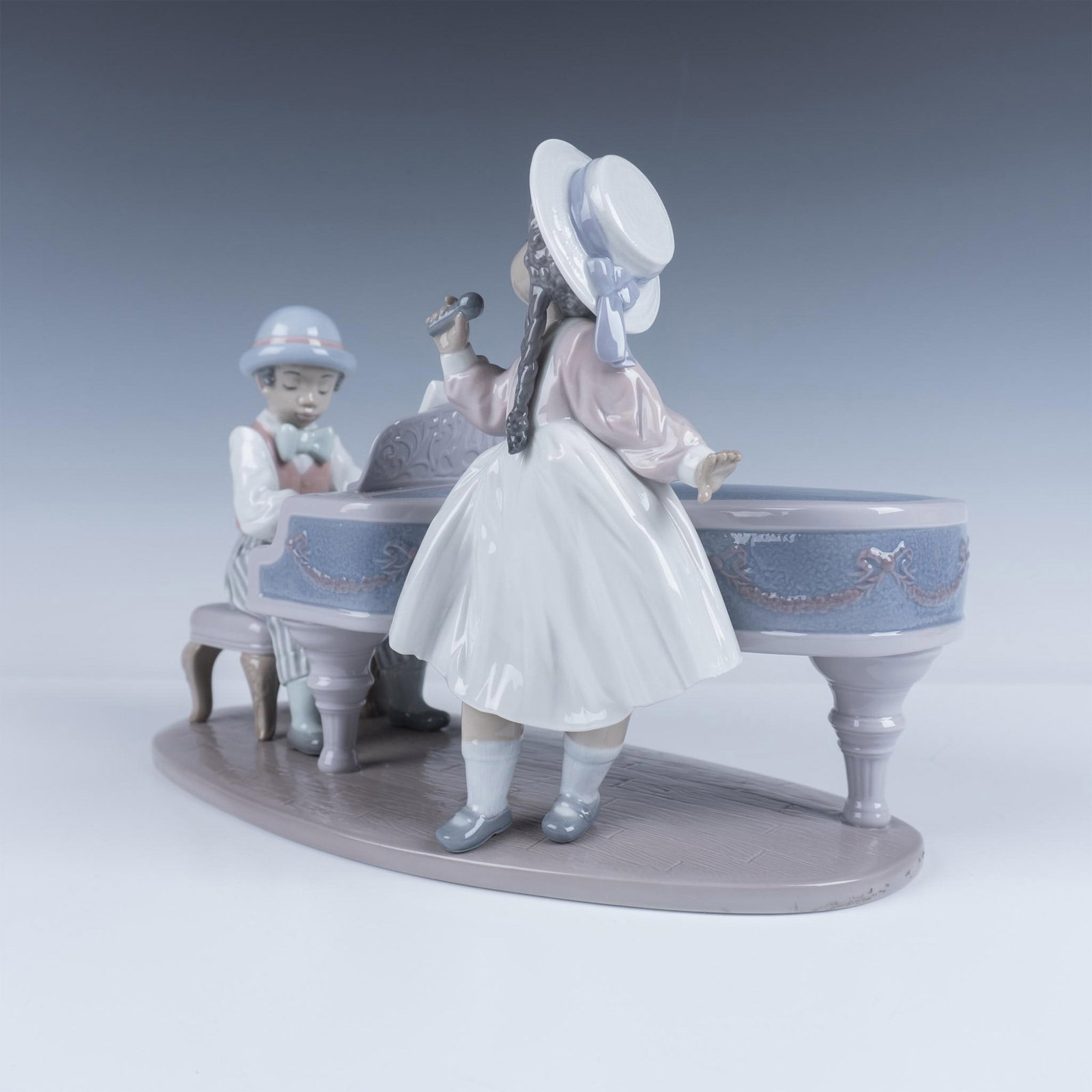 Lladro Porcelain Figurine, Jazz Duo: Glossy enchanting sculpture of a pianist and a singer, enjoying the music. Colored in lavender and rose. Lladro backstamp. 1005930. This item has its original box 17.5"L x 11"W x 10.75"H. Artist: Anto