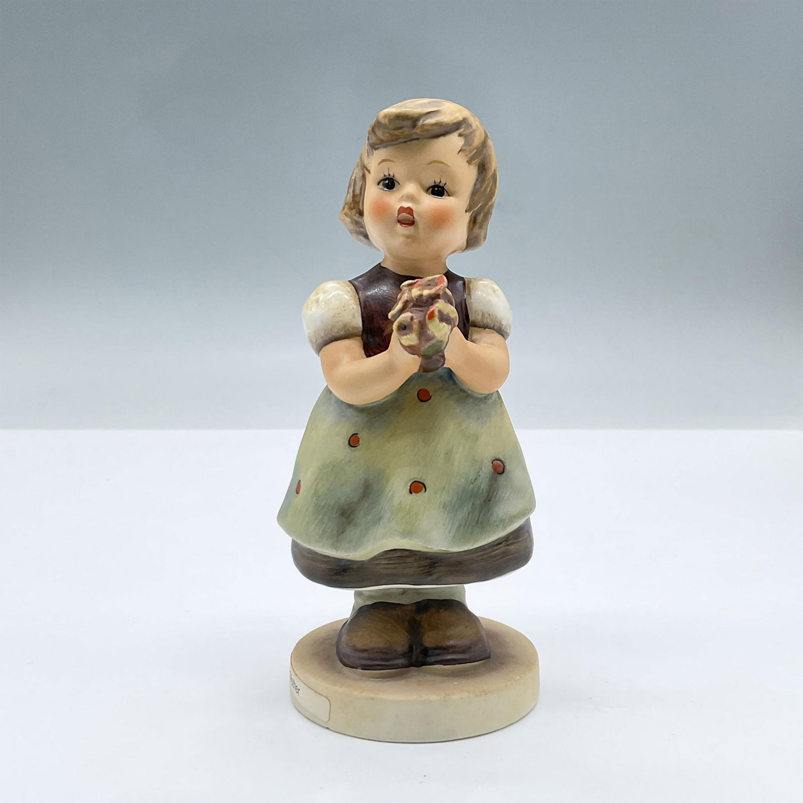 Goebel Hummel Porcelain Figurine, For Mother 257: A tender figure of a little girl in a dress holding flowers. Goebel Hummel backstamp. Issued: 20th century Dimensions: 2.5"L x 2.25"W x 5.25"H Manufacturer: Goebel Hummel Country of Origin: Germany