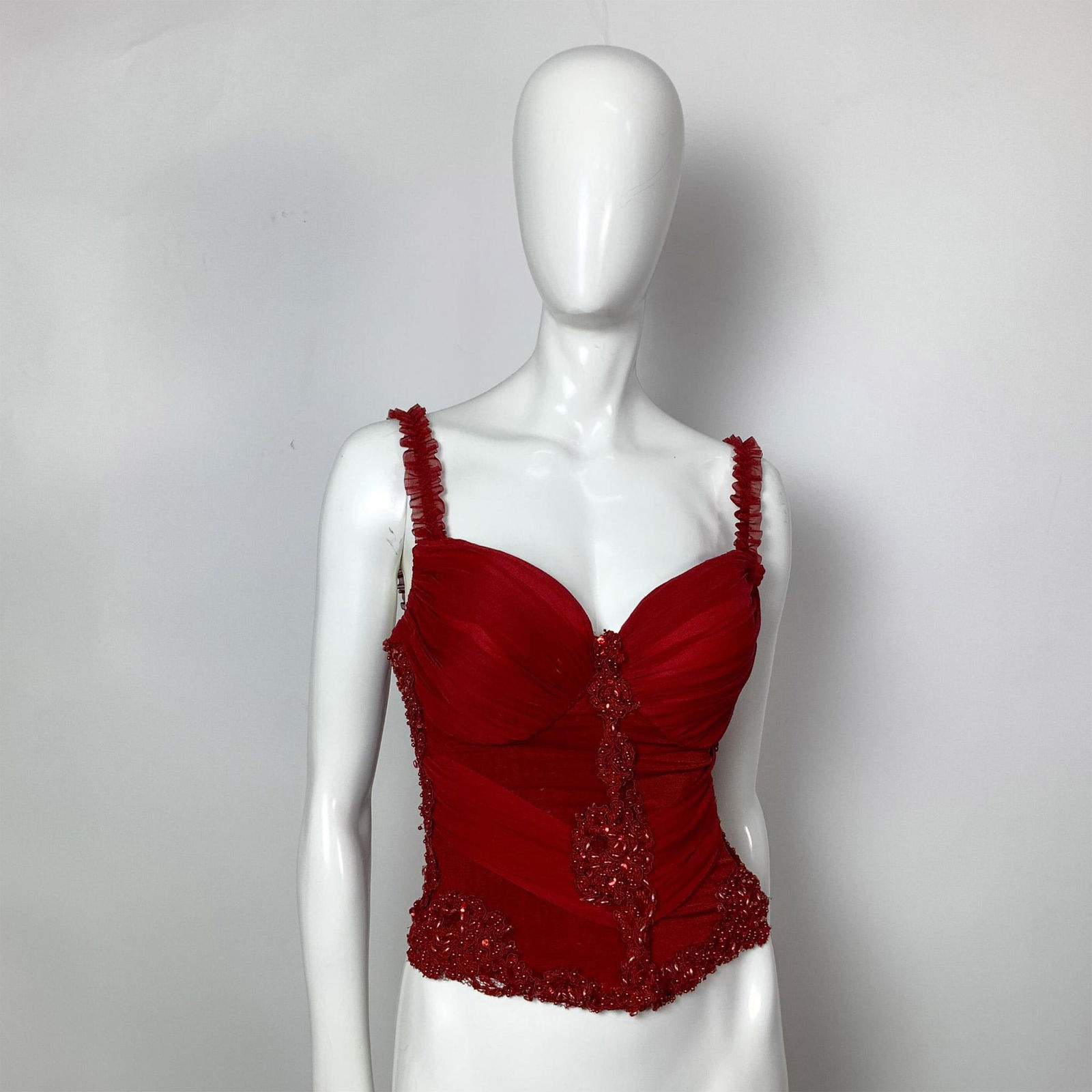 Consuelo Celemin Red Ruched Mesh Lace Beaded Bustier: A vintage ruched red mesh bustier adorned with red lace and embellished with sequins and beads. Bust: 14"W. Waist: 10"W. Full length: 16"L. All measurements are approximate. Issued: c. 1980 Dimensions