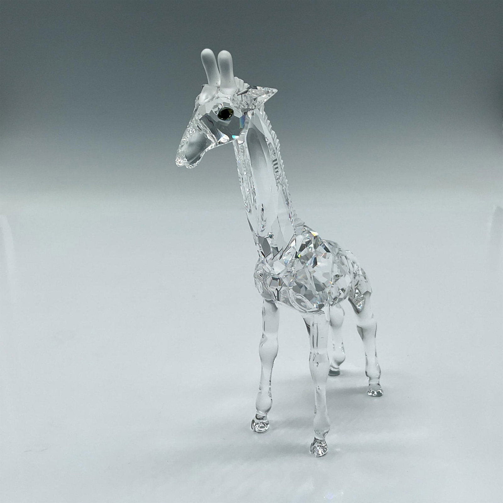 Swarovski Crystal Figurine, Giraffe Baby: Clear faceted crystal body, smooth tail and legs, amber crystal eyes with frosted mane and antlers. Swarovski backstamp. 236717. Artist: Michael Stamey Issued: 1999 - 2007 Dimensions: 4"L x 1.5"W x 5.