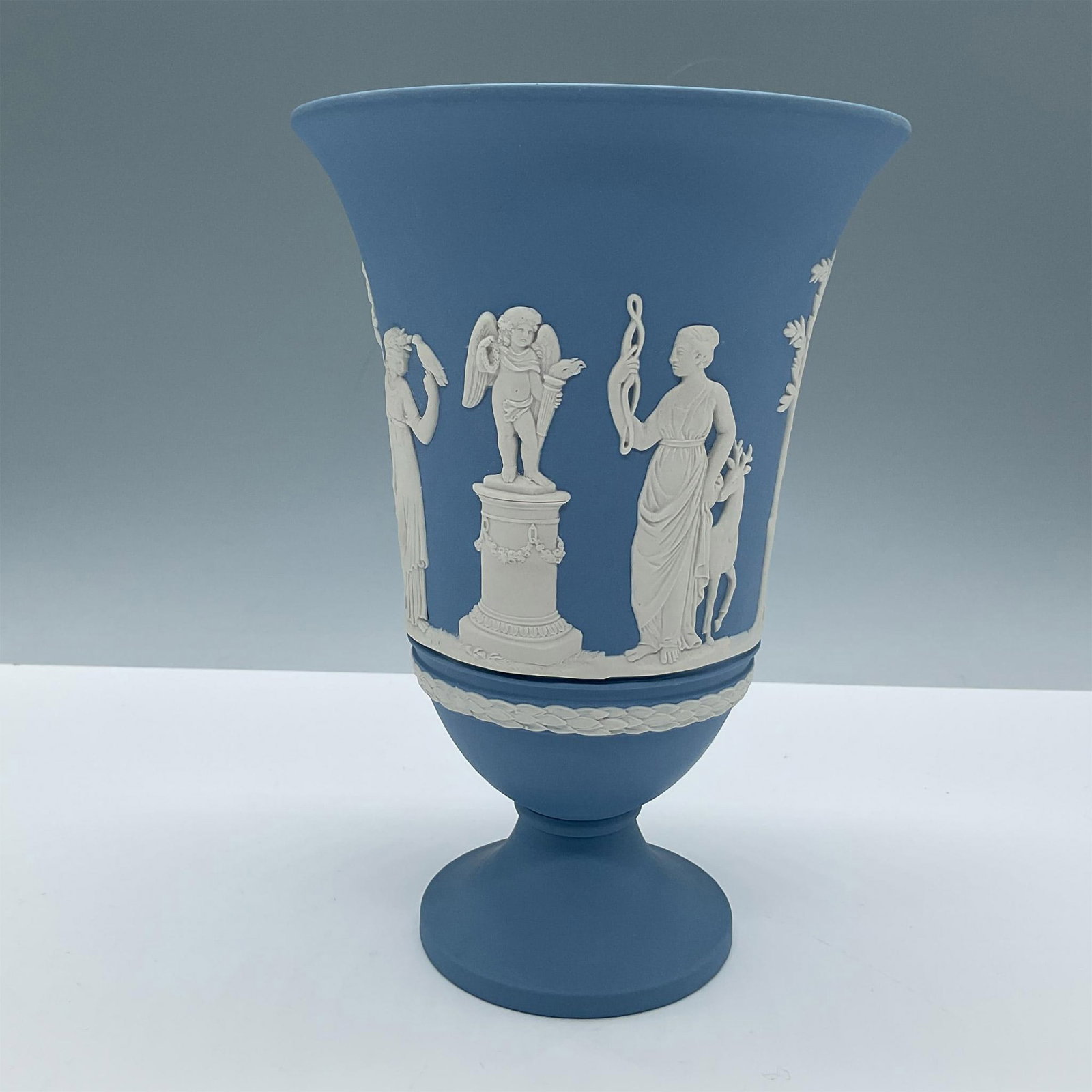 Wedgwood Pale Blue Jasperware Footed Vase: Beautiful pale blue English pottery flower vase. In raised white reliefs: Sacrifice figures and peace offerings. Wedgwood impressed mark on base. Issued: Antique Dimensions: 7.5''H x 5.25''dia Manufac