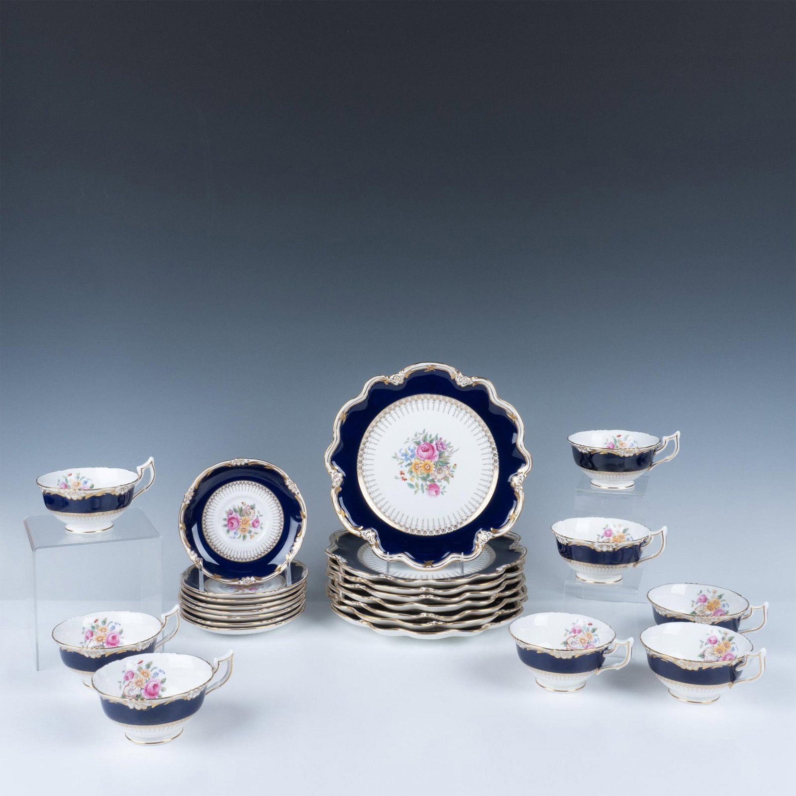 24pc Coalport Bone China Trio Tea Set: An elegant set of eight teacups, saucers, and tea plates adorned with a royal blue curved band and gilted embellishments, featuring floral bouquets in the center. Coalport backstamp. Tea plate: 9.5"W.