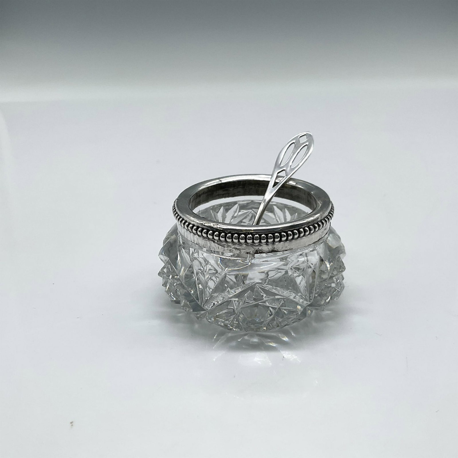 Cut Crystal Salt Cellar with Silver Rim and Spoon: Exquisite cut crystal with 925 sterling silver beaded rim with pierced serving spoon marked Sterling. 82g. Issued: 20th century Dimensions: 1.25"H x 2" dia.