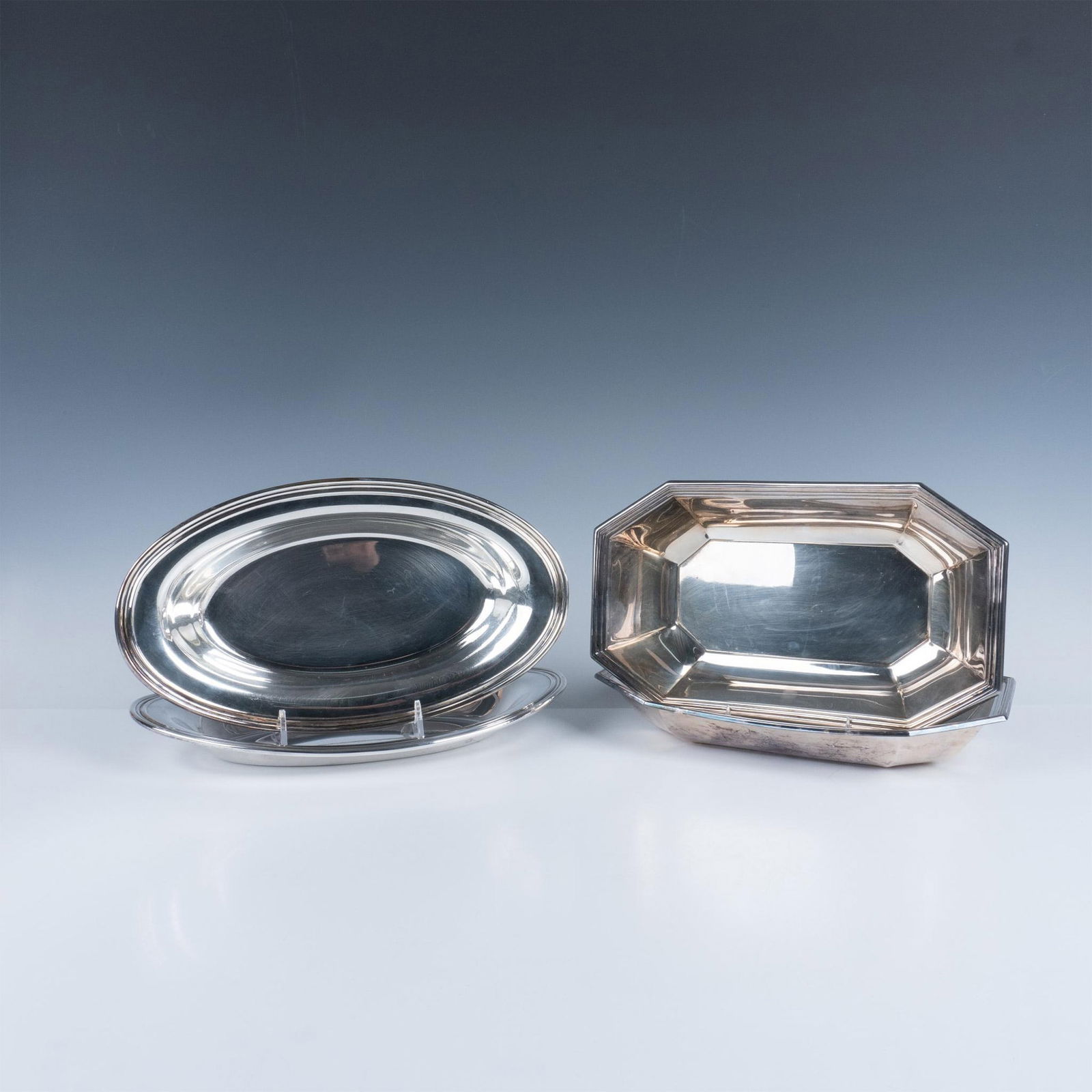 4pc Vintage Silver-Plated Serving Bread Trays: This lovely silver-plated tableware set includes a pair of matching sleek oval trays and a pair of matching Art Deco angular trays. WM Rogers marking. Wallace Silversmiths marking and sticker. Largest