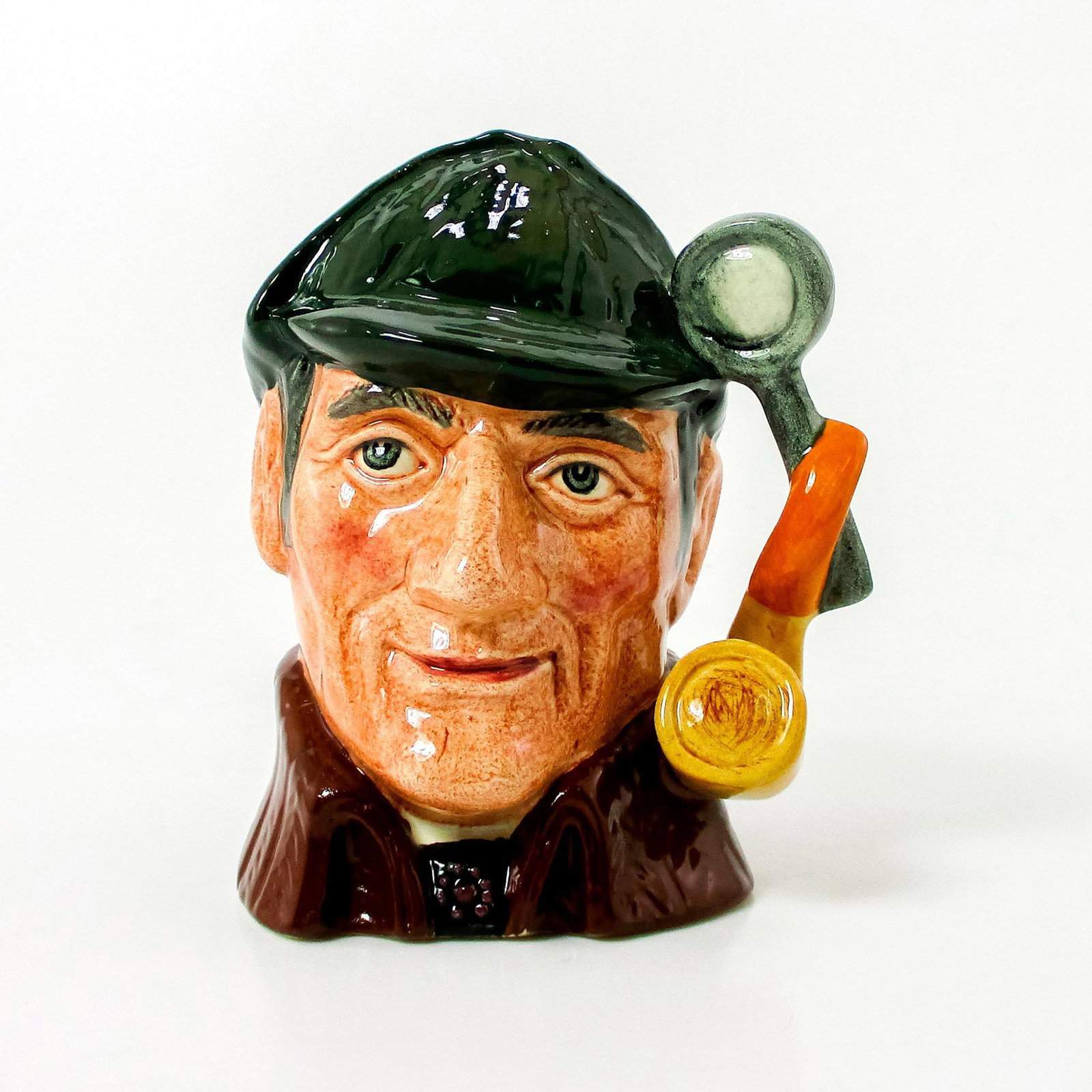 Sleuth D6635 - Small - Royal Doulton Character Jug: Variation One. Dark green deerstalker hat; brown cloak. Arthur Conan Doyle (1859 - 1930), an unsuccessful doctor, published the first of his widely popular detective stories in 1887. The amateur sleut