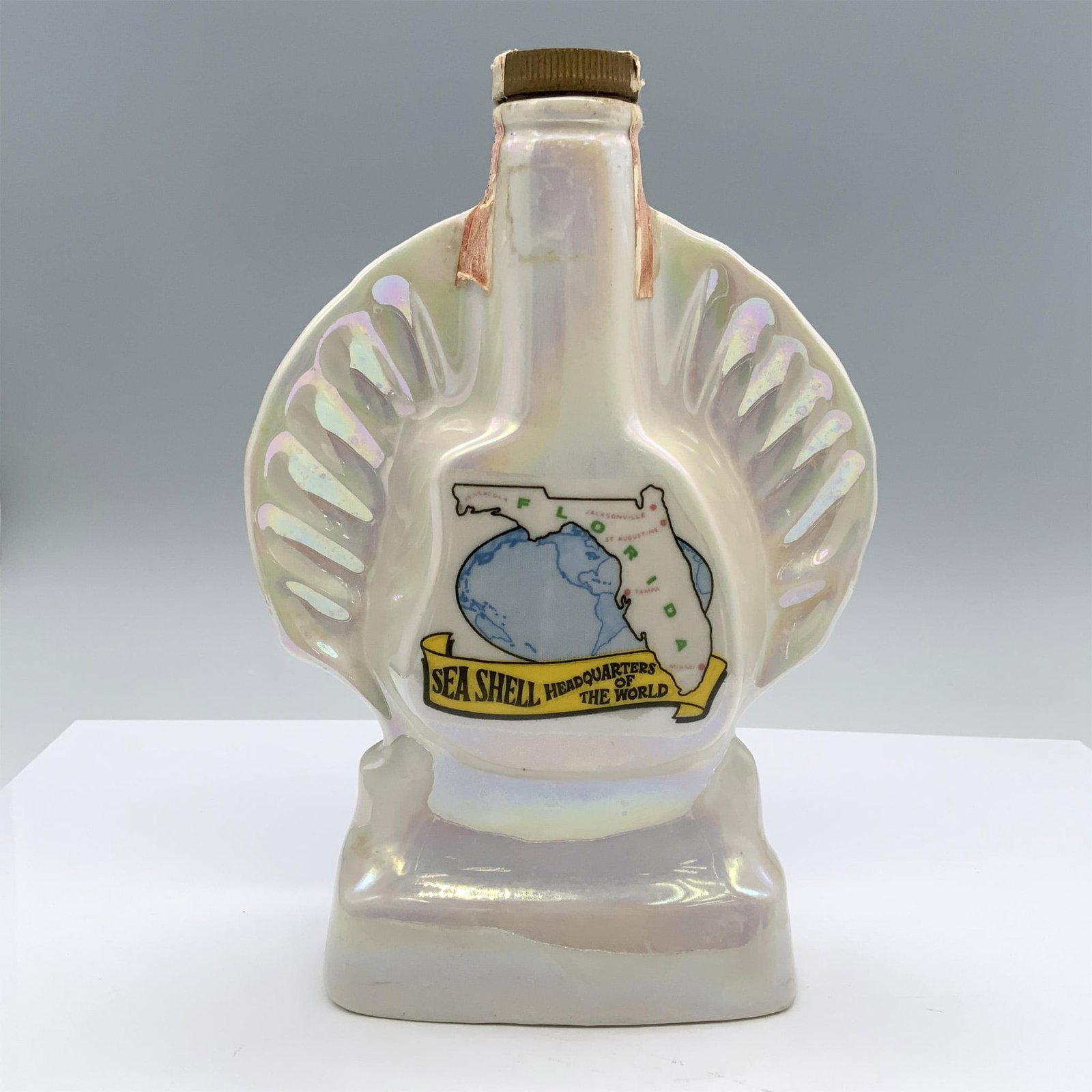 Vintage Jim Beam Porcelain Florida Advertising Decanter: Lovely iridescent porcelain shaped like a clam shell with map of Florida on the front. Jim Beam and Regal China backstamp. Issued: 1968 Dimensions: 7"L x 3.5"W x 10"H Manufacturer: Regal China Corp. C