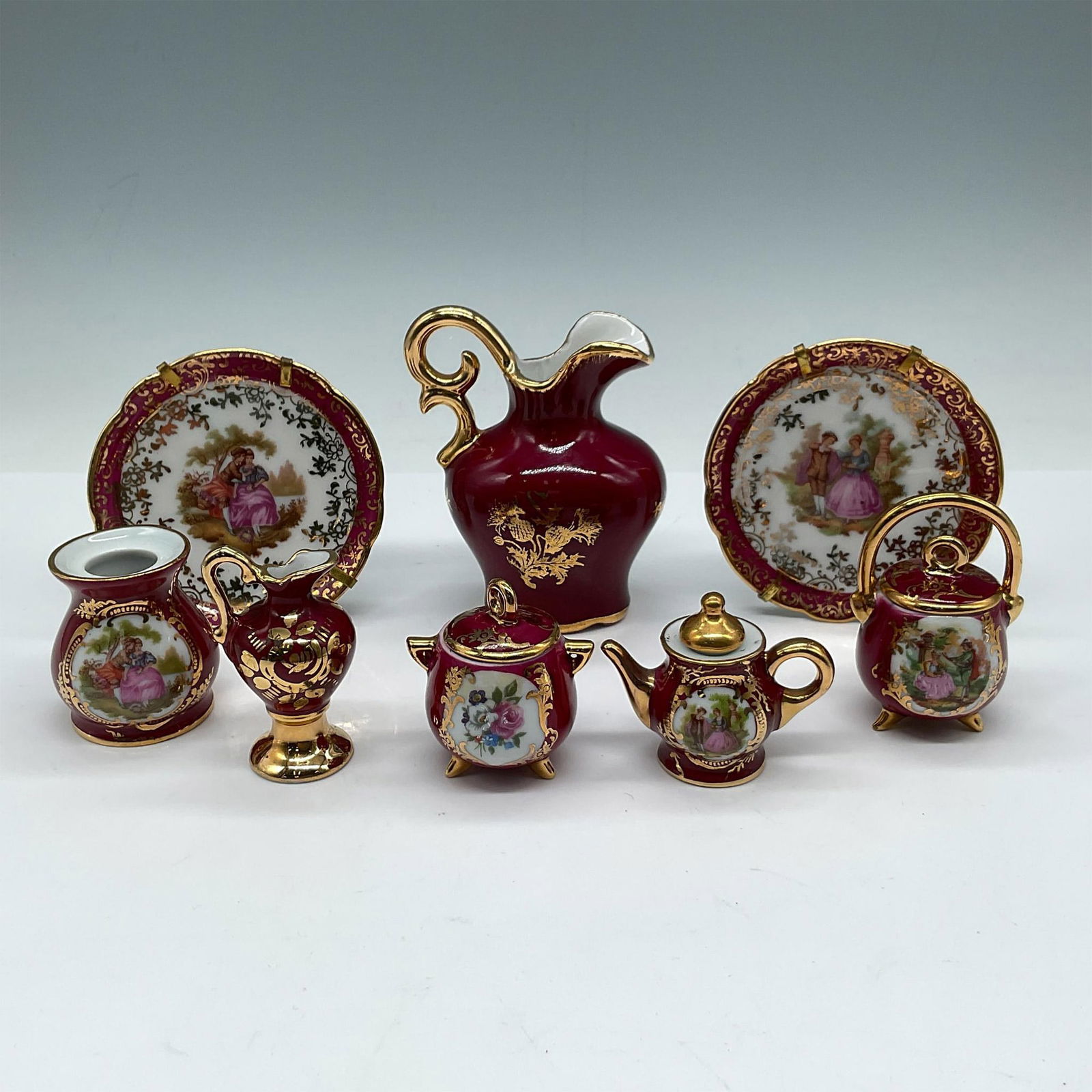 8pc FM & Castel Limoges Porcelain Miniature Collection: Decorative pieces in burgundy porcelain adorned with hand painted scenes and gilt accents. Collection includes 2 plates; pitcher; candle holder; kettle with cover; teapot; pot with cover; and small pi