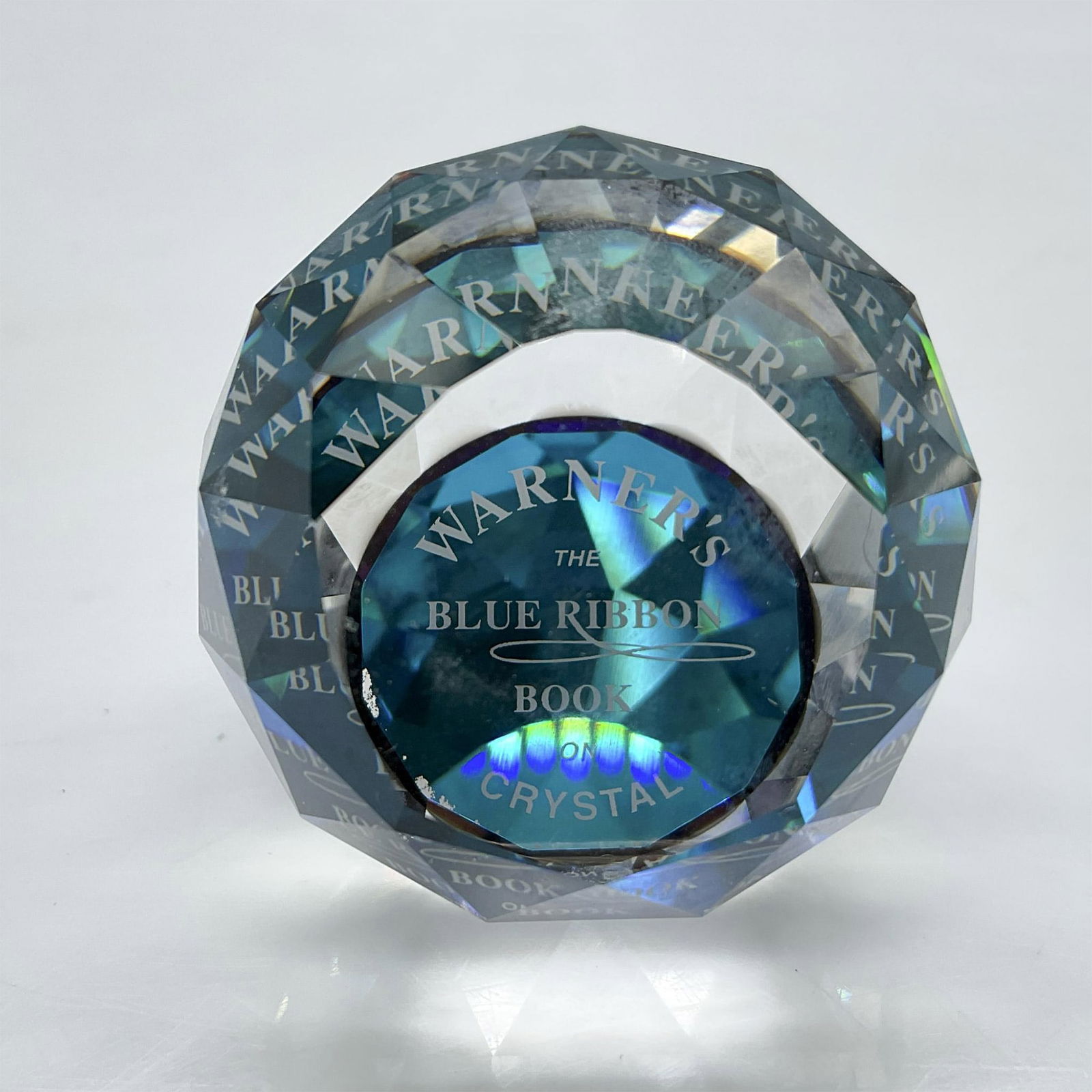 Swarovski Crystal Paperweight, Warner's Blue Ribbon Book: Round faceted Limited Edition crystal designed with a nod to Warner's Book. Felt bottom protects base. Swarovski backstamp. 9406 040 002. This item has its original box: 3.5"L x 3.5"W x 2.5"H. Issued: