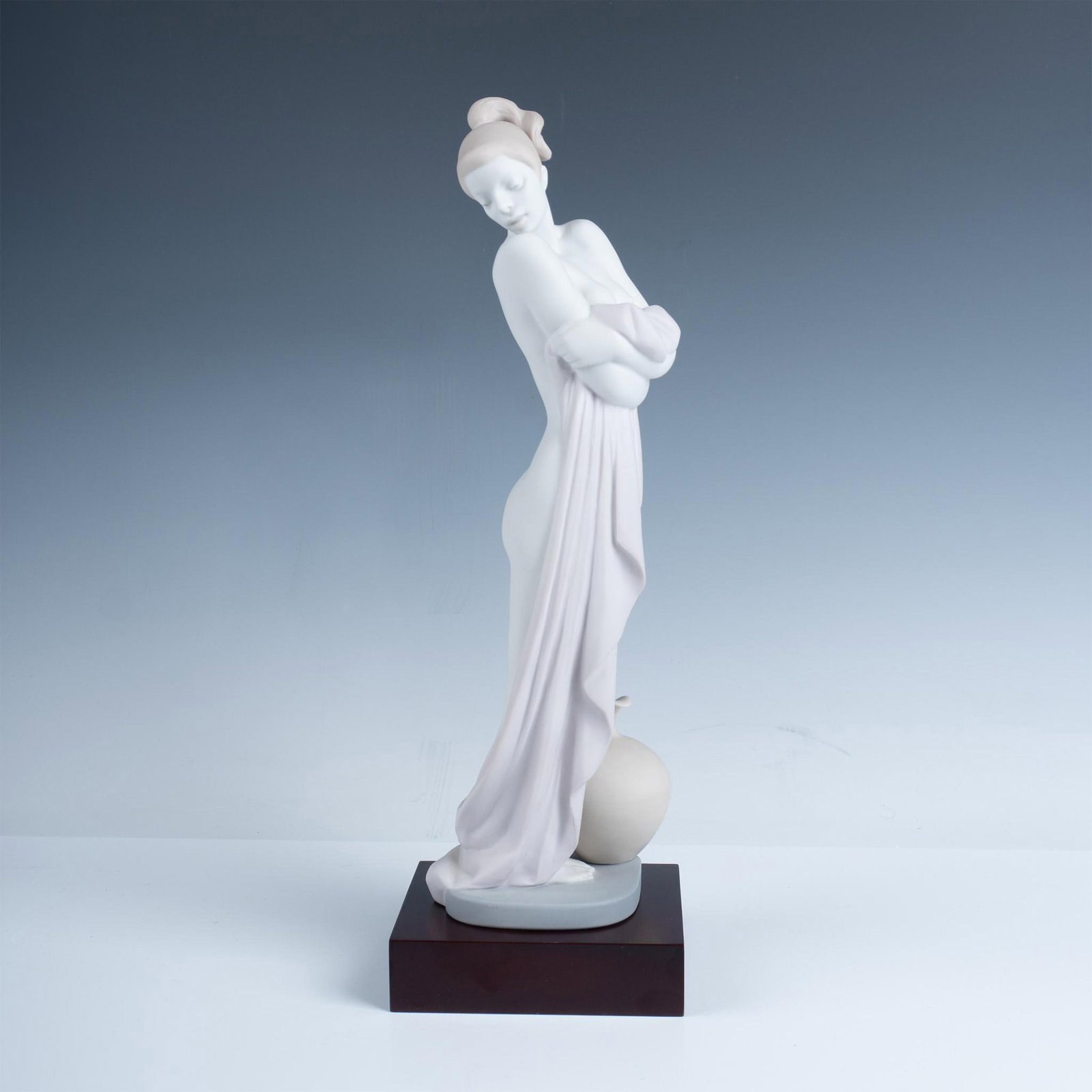 After The Bath 01013023 - Lladro Porcelain Figurine: Matte finish porcelain figurine depicting a nude woman elegantly draped with a towel, standing on a square base. Lladro backstamp. This item has its original box. Box measures: 8.25"L x 7"W x 6.75"H. 