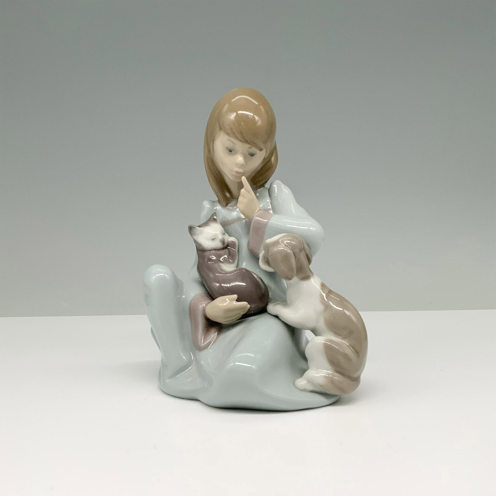 Cat Nap 01005640 - Lladro Porcelain Figurine: Glossy figure of a young lady holding her cat while her dog playfully joins them. Lladro backstamp. This item has its original box. Box measures: 8.25"L x 5.5"W x 4.75"H. Artist: Juan Huerta Issued: 1