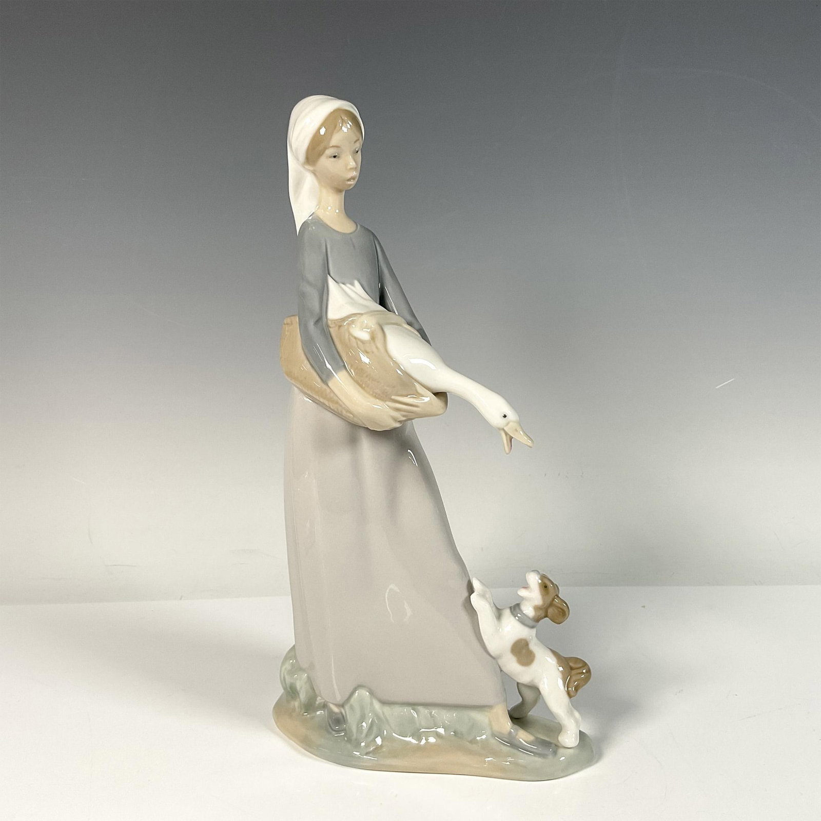 Girl with Goose and Dog 1004866 - Lladro Porcelain Figurine: Glossy porcelain figure capturing a humorous daily scene of a girl, a goose and a dog watching each other. Lladro backstamp. Artist: Fulgencio Garcia Issued: 1970-1992 Dimensions: 5.75"L x 3.25"W x 11