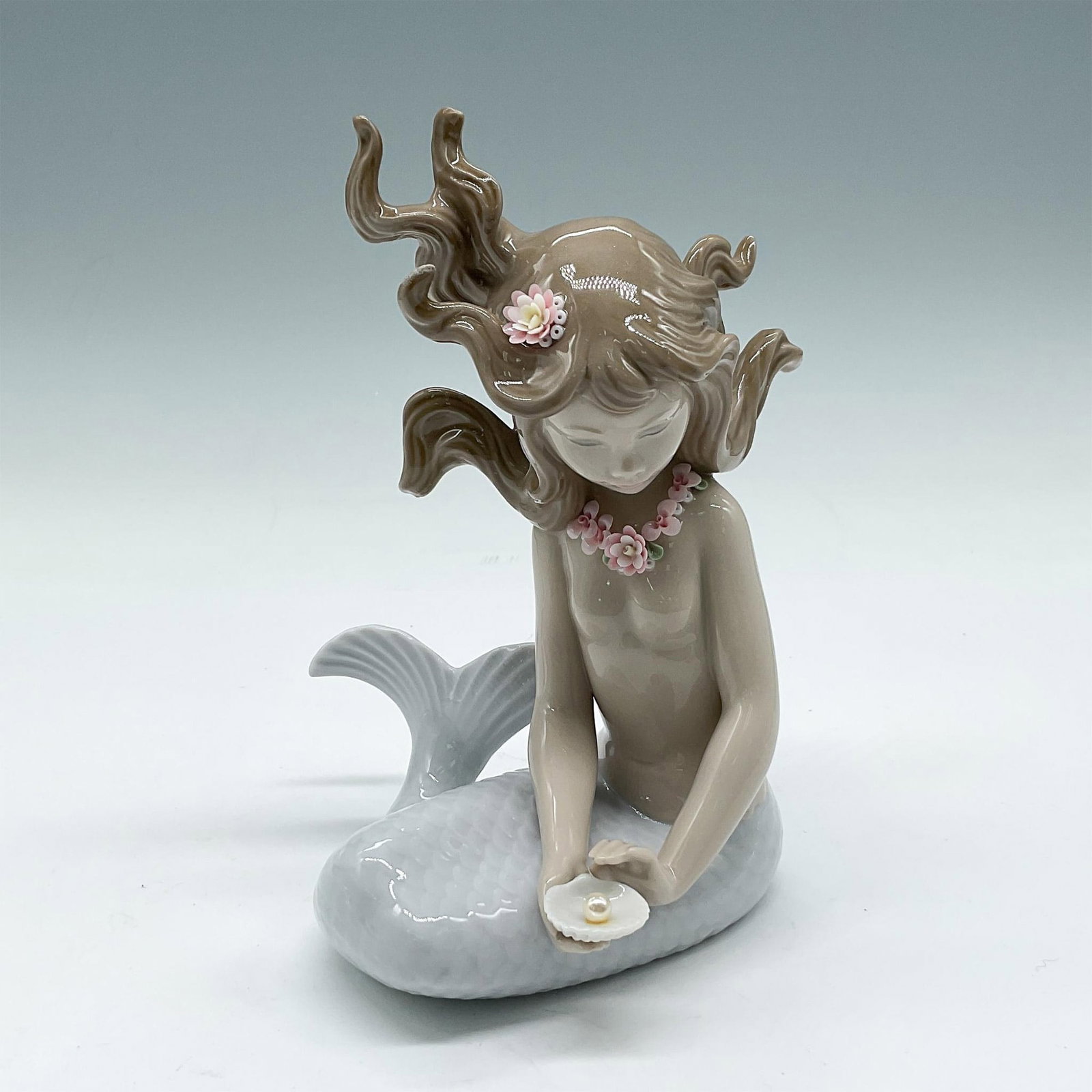 Mirage 01001415 - Lladro Porcelain Figurine: Lovely sea mermaid admiring a pearl. Colored in brown, pink and blue. Base is not included. Lladro backstamp. This item has its original box: 8"L x 9"W x 5.5"H. Artist: Jose Puche Issued: 1982 Dimensi