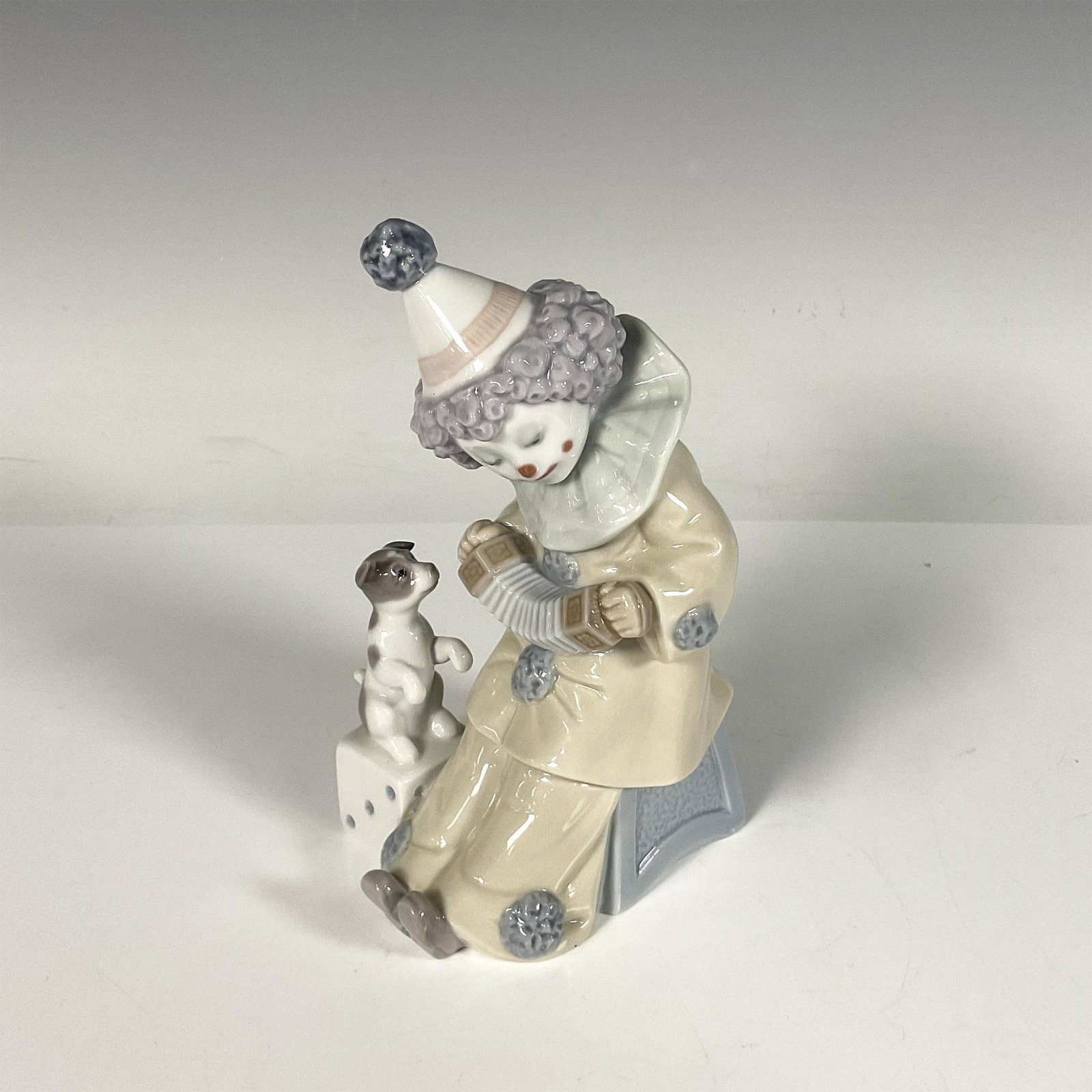 Pierrot with Concertina 1005279 - Lladro Porcelain Figurine: Glossy porcelain figure of a child clown playing an accordion, while a dog appreciates the concert. Lladro backstamp. Artist: Jose Puche Issued: 1985-2007 Dimensions: 3.5"L x 3"W x 6"H Manufacturer: L