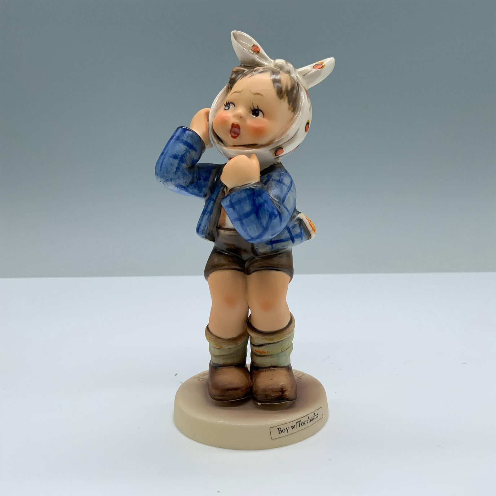 Goebel Hummel Figurine, Boy with Toothache: Hand painted porcelain with matte finish features a distressed boy who is wearing a plaid blue jacket and a polka-dotted scarf around his head. M.I. Hummel impressed. Goebel backstamp. Issued: 1951-20