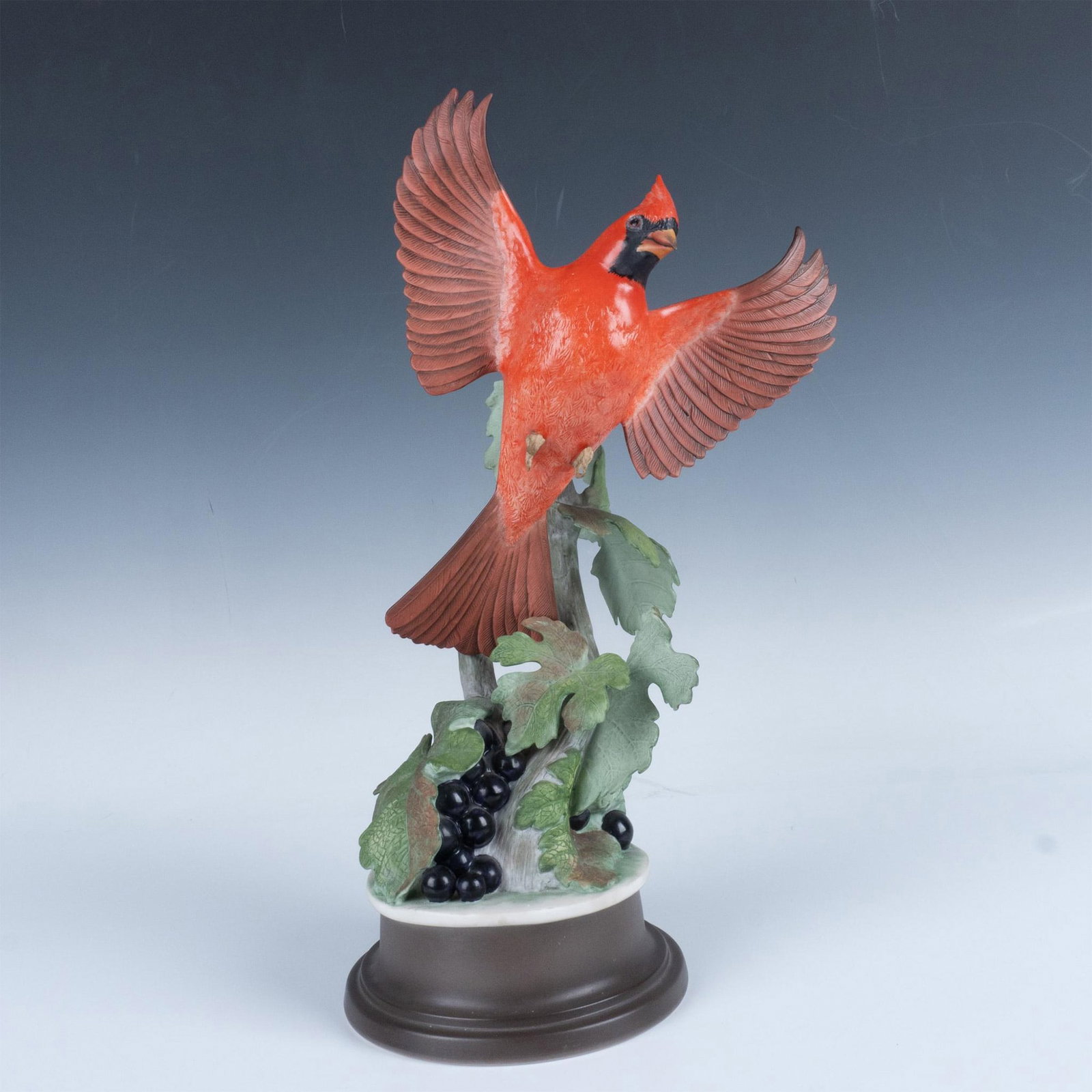 Boehm Porcelain Figurine, Cardinal 415, Male: A stunning red cardinal takes flight from a grapevine, its wings spread wide in a display of vibrant color and grace. Boehm backstamp. Marked USA. Dimensions: 9"L x 7"W x 14.75"H Manufacturer: Boehm C