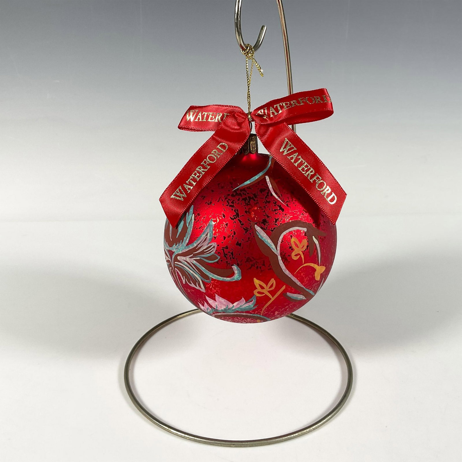 Waterford Floral Ball Ornament, Holiday Heirlooms: Handcrafted glass bauble adorned with hand-painted flowers in pink, blue, and yellow shades that gracefully curve around the ornament. The matte red finish, with intricate details, makes the motif sta