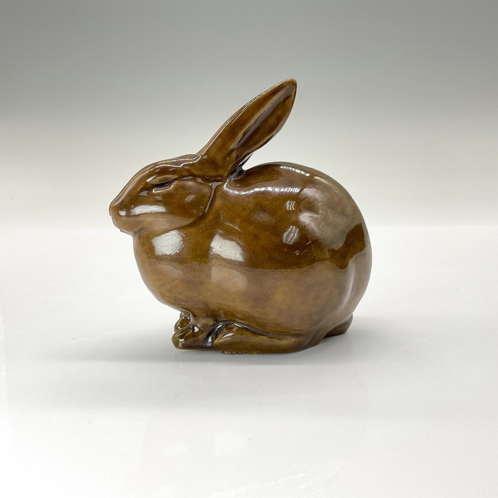 Rookwood Present Day Pottery Animal Figurine, Brown Rabbit: Adorable crouched rabbit crafted from the original master mold #6160 from 1928. Finished in a high-gloss brown glaze. Rookwood backstamp. This item has its original box that measures 5.5"L x 4"W x 3.7