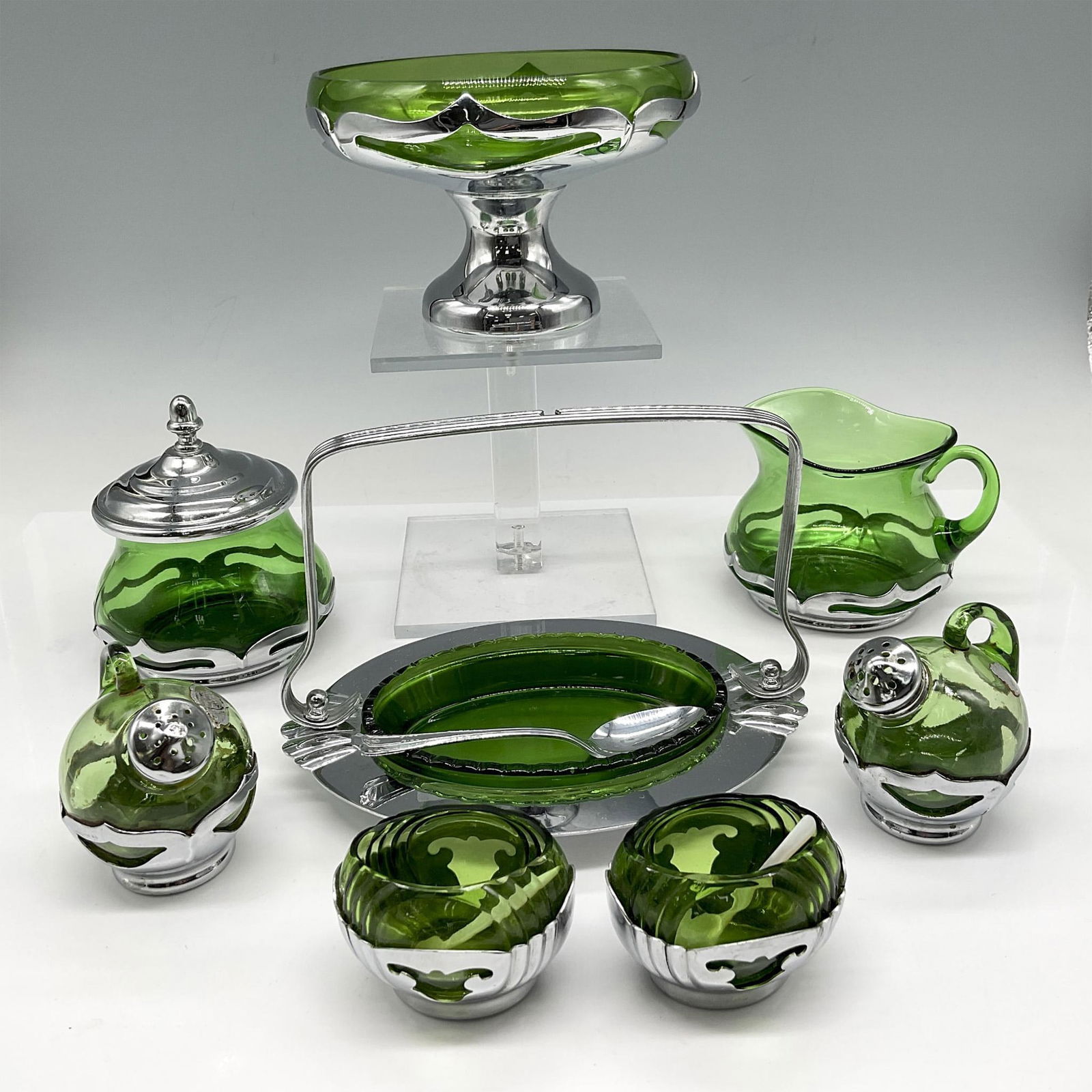 8pc Farber Brothers Green Chrome Serveware: Emerald green glass with chrome cased exterior carriers. Lot includes jelly dish with serving spoon; footed fruit bowl; creamer jug; sugar bowl with lid; set of shakers; and 2 salt cellars. Farber Bro