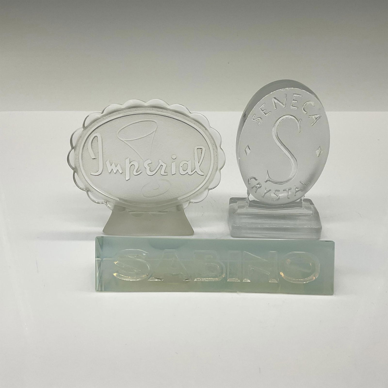 3pc Mid Century Glass Companies Dealer Signs / Plaques: This collection includes clear and frosted signs from Imperial Glass, Seneca Crystal, and Sabino Glass crafted in opalescent glass. The largest piece measures 3.75"L x 1.5"W x 3.25"H. Issued: 20th cen