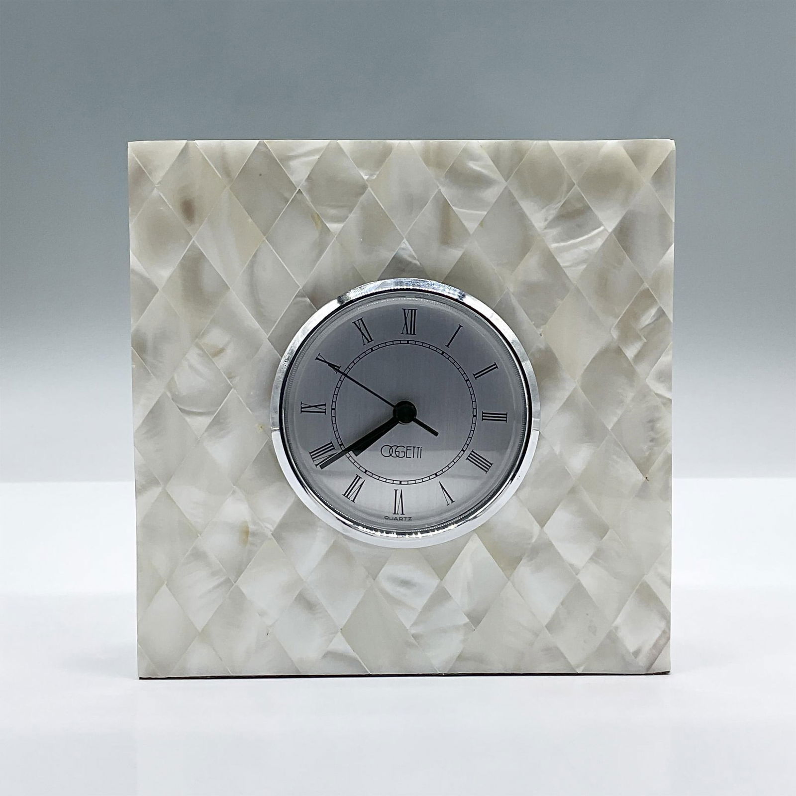 Oggetti Mother of Pearl Table Clock: This lustrous cuboid with a mother of pearl appearance holds a circular battery operated removable clock. Oggetti mark to the face of the clock. Issued: 20th century Dimensions: 5.5'L x 1.75"W x 5.5"H