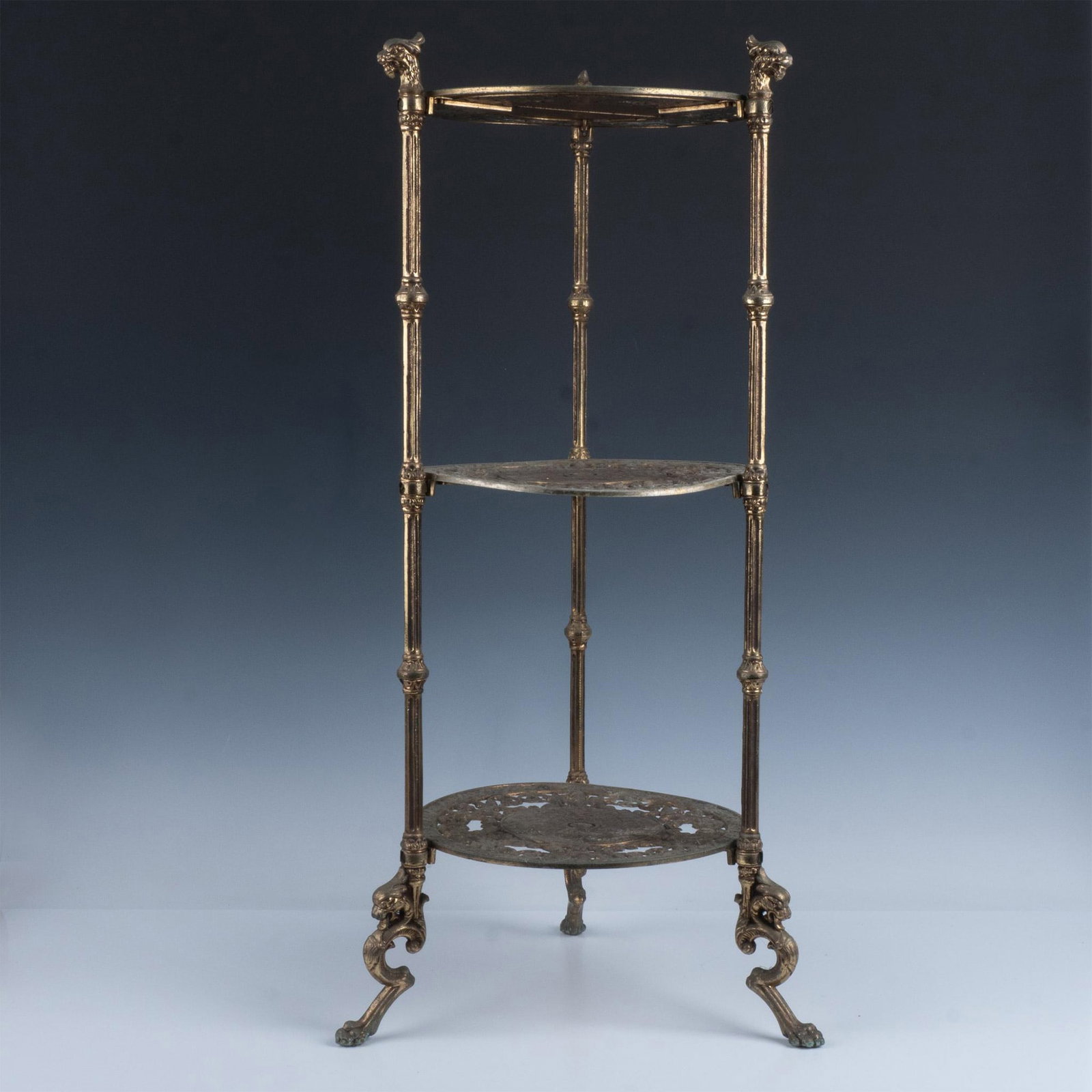 Ornate Brass 3 Tier Griffin Head Stand: Round disc designed with cherubs and griffins supported by 3 legs with griffin head and claw foot. Issued: 20th century Dimensions: 29.5"H x 14" dia.