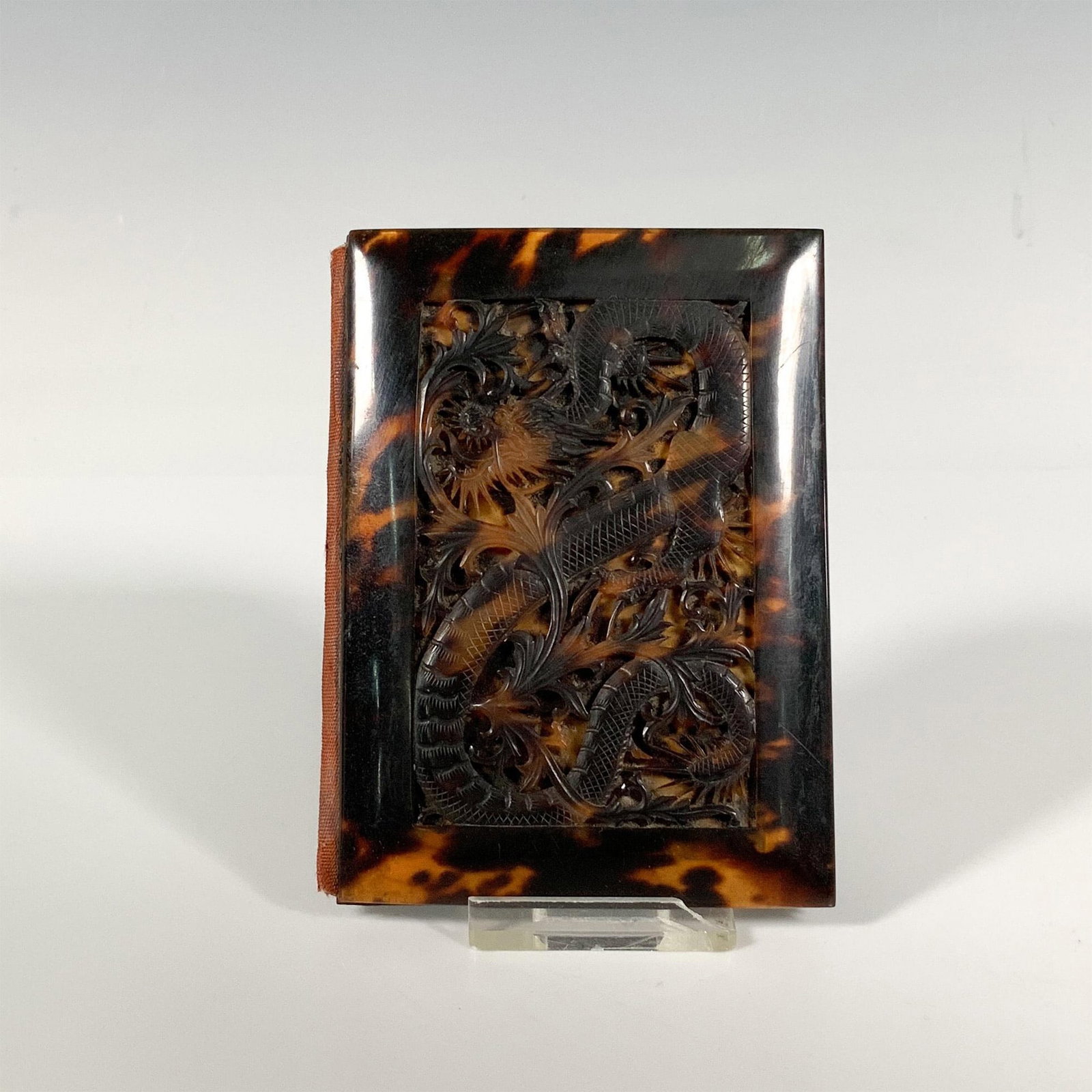 Mottled Amber and Silk Carved Dragon Card Case: A stylish mottled amber-colored card case lined with dark purple silk, adorned with a stunning, carved dragon on the front. Issued: 20th century Dimensions: 3"L x 0.5"W x 4"H