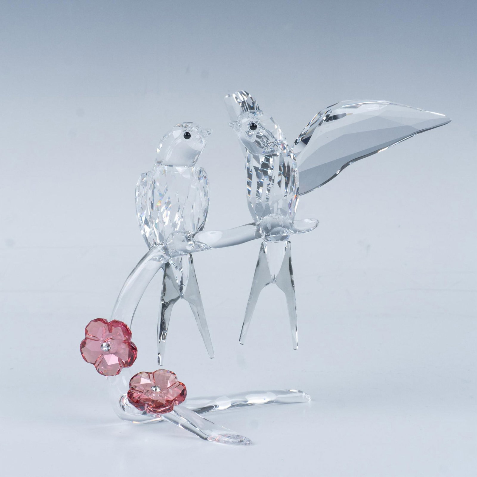 Swarovski Crystal Figurine, Swallows 5475566: Two swallows perch on a tree branch adorned with blooming red flowers, as one swallow spreads its wings in a charming display to impress the other. Swarovski backstamp. This item has its original box.
