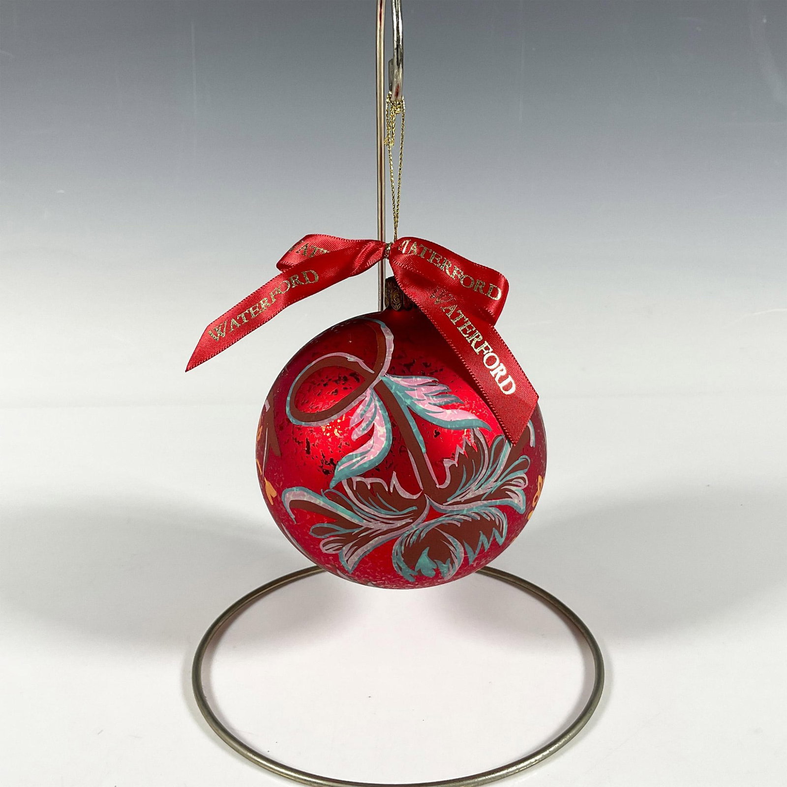 Waterford Floral Ball Ornament, Holiday Heirlooms: Handcrafted glass bauble adorned with hand-painted flowers in pink, blue, and yellow shades that gracefully curve around the ornament. The matte red finish, with intricate details, makes the motif sta