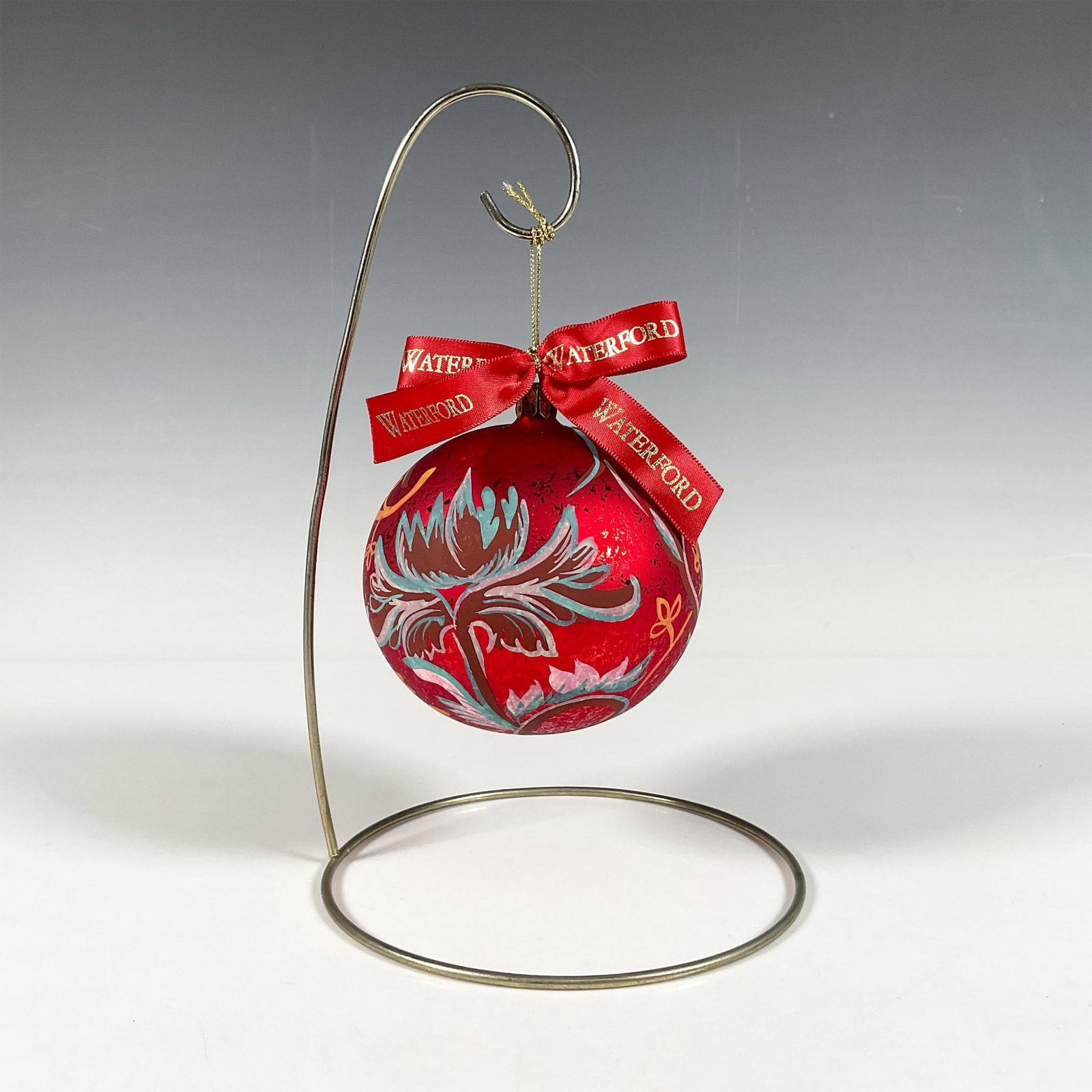 Waterford Floral Ball Ornament, Holiday Heirlooms: Handcrafted glass bauble adorned with hand-painted flowers in pink, blue, and yellow shades that gracefully curve around the ornament. The matte red finish, with intricate details, makes the motif sta