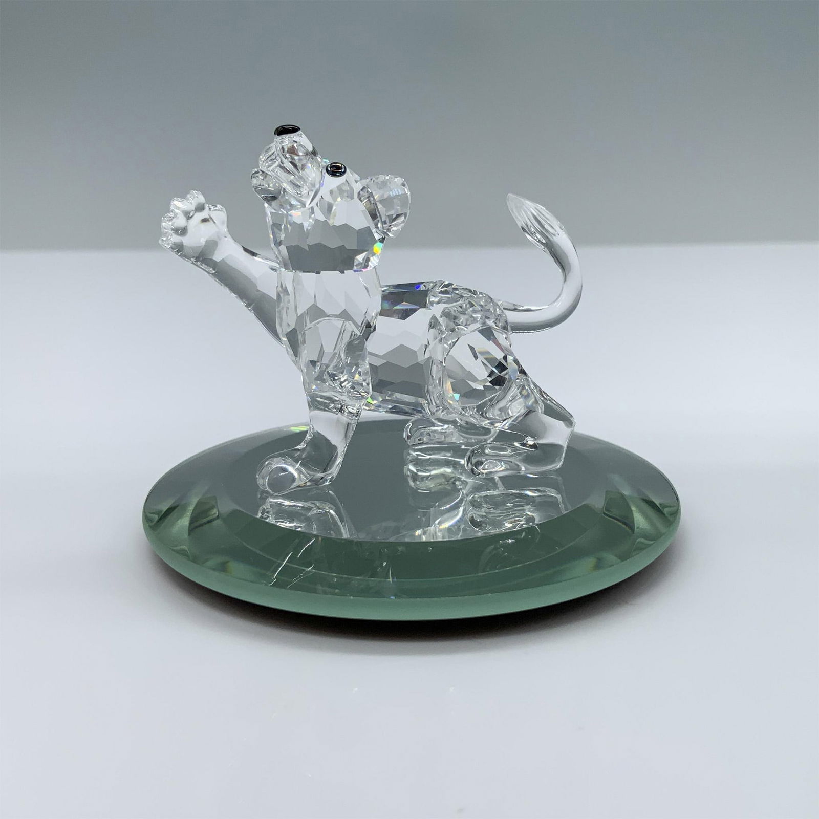 Swarovski Crystal Figurine, Lion Cub: Beautiful little lion in a playfully posture with one his paw up in the air. Swarovski swan mark. This item has its original box. Box measures: 4.75"H x 3.25" dia. 210460. Included mirror base, measur