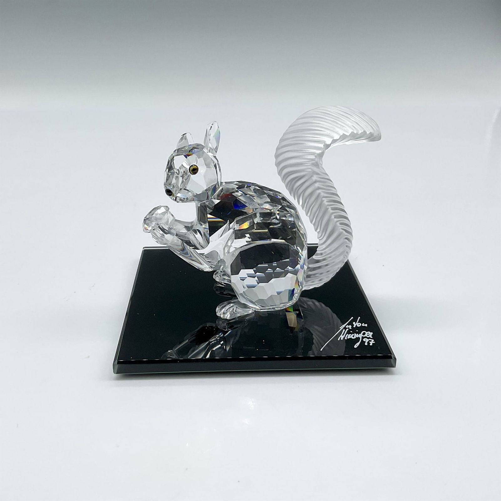 Swarovski Crystal Figurine Squirrel 10th Anniversary + Base: Clear crystal figural holding a nut, amber eyes, black nose and frosted, grooved tail. Swarovski backstamp. 208433. This item has its original box: 4"L x 4"W x 3.25"H. This item has a signed and dated