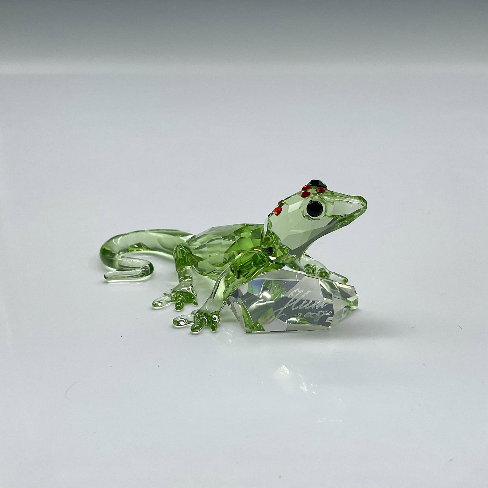 Swarovski Crystal Figurine, Gecko, Signed: Limited edition event piece made from green crystal, with black eyes, and red stones on the top of his head holding a clear chaton. Signed by artist. Swarovski backstamp. 905541. Item comes in origina