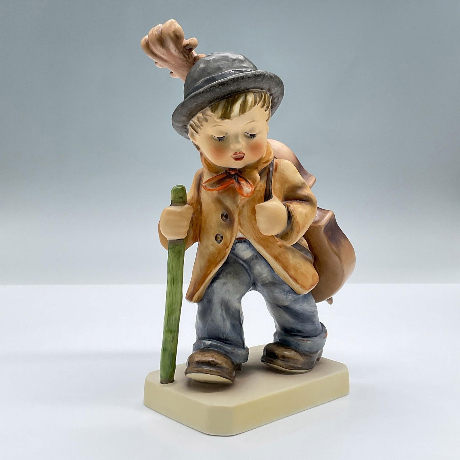 Goebel Hummel Figurine, Little Cellist: Features a porcelain figure of a boy carrying a cello and walking stick. Marked Goebel 89/II. Issued: 20th century Dimensions: 4.25"L x 3"W x 7.5"H Manufacturer: Goebel Hummel Country of Origin: Germa