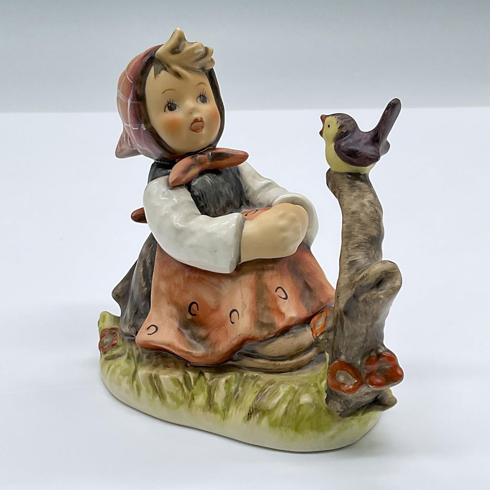 Goebel Hummel Figurine, In Tune: A tender porcelain figure of a seated girl singing with along with a bird. Marked Goebel 414. Issued: 1979 Dimensions: 4.25"L x 2.5"W x 4.25"H Manufacturer: Goebel Hummel Country of Origin: Germany