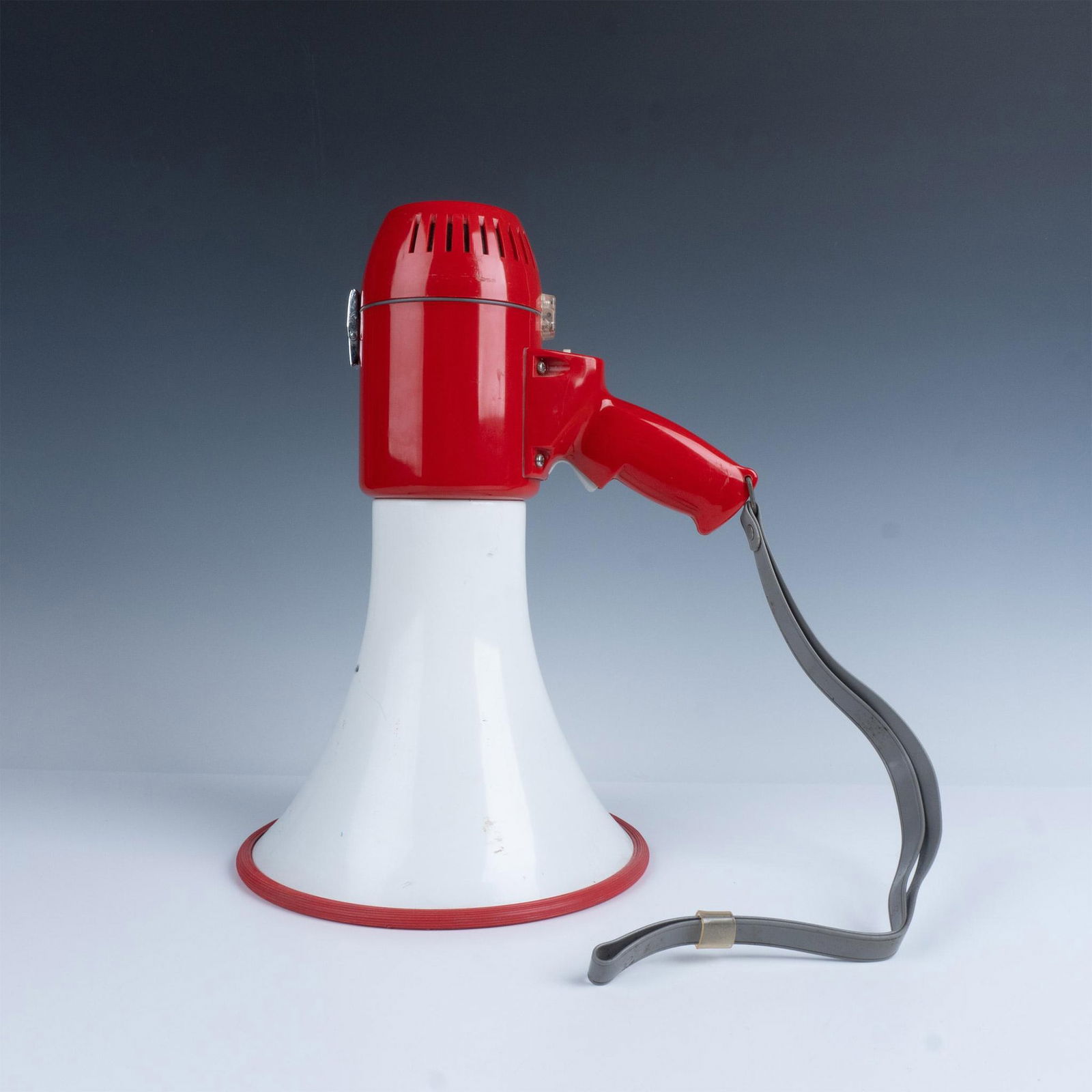 Sireno Loudhailer Megaphone: A vibrant white and red megaphone, designed with a sleek angled handle for easy grip. Marked Sireno Loudhailer. Marked Japan. Dimensions: 14"L x 9"W x 11.75"H Manufacturer: Sireno Country of Origin: J