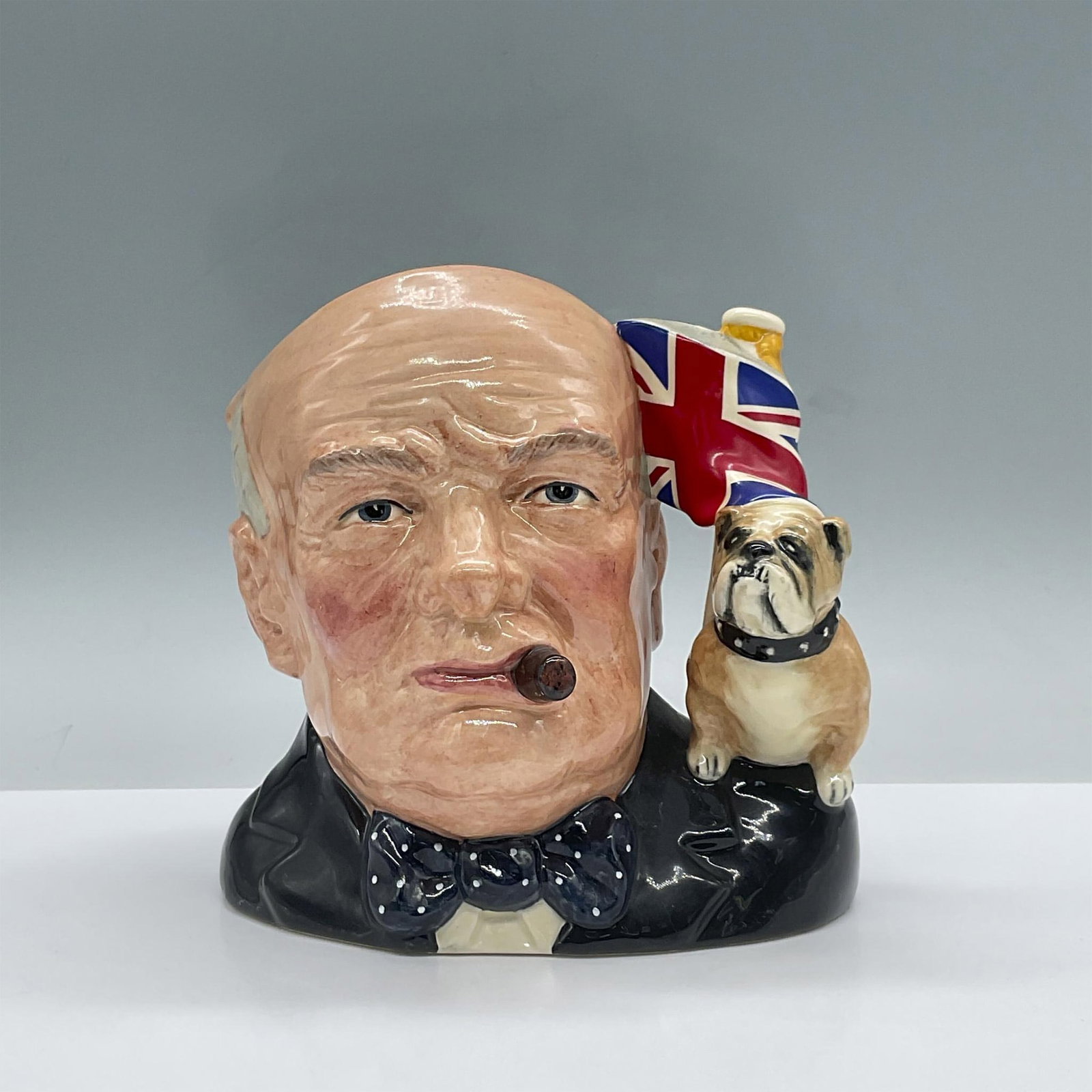 Winston Churchill D6907 (Union Jack and Bulldog Handle) - Large - Royal Doulton Character Jug: Style One. Black, brown and white coloration. Includes certificate of authenticity. Royal Doulton backstamp. Artist: Stanley J. Taylor Issued: 1992 - 1992 Dimensions: 7"H Manufacturer: Royal Doulton