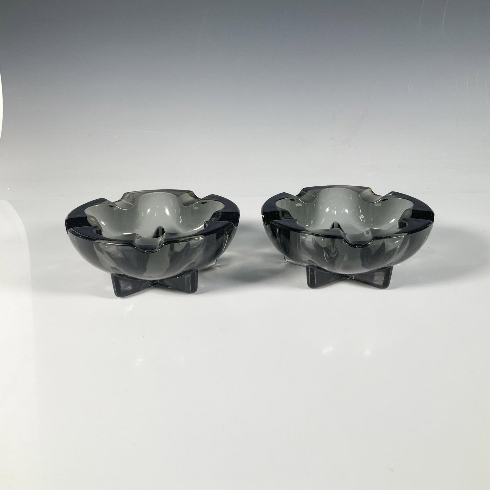 Pair of Heisey Dawn Lodestar Ashtrays: This stunning ashtray duo features star shaped bases and a charcoal gray hue. Heisey marking. Each ashtray measures: 5.25"W x 2"H. Issued: 1955-1957 Dimensions: See Description Manufacturer: Heisey & 
