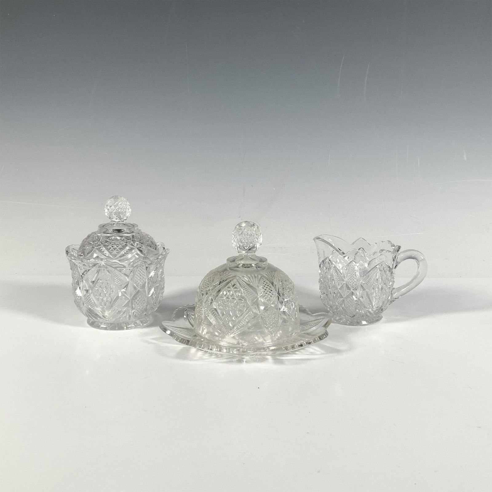 3pc U.S. Glass Co. Pennsylvania EAPG Serveware: An exquisite set featuring a round butter plate with lid, a creamer, and a sugar bowl with lid, all in a stunning diamond and geometric cut glass pattern. Butter plate with lid: 5"W x 3"H. Creamer: 3.