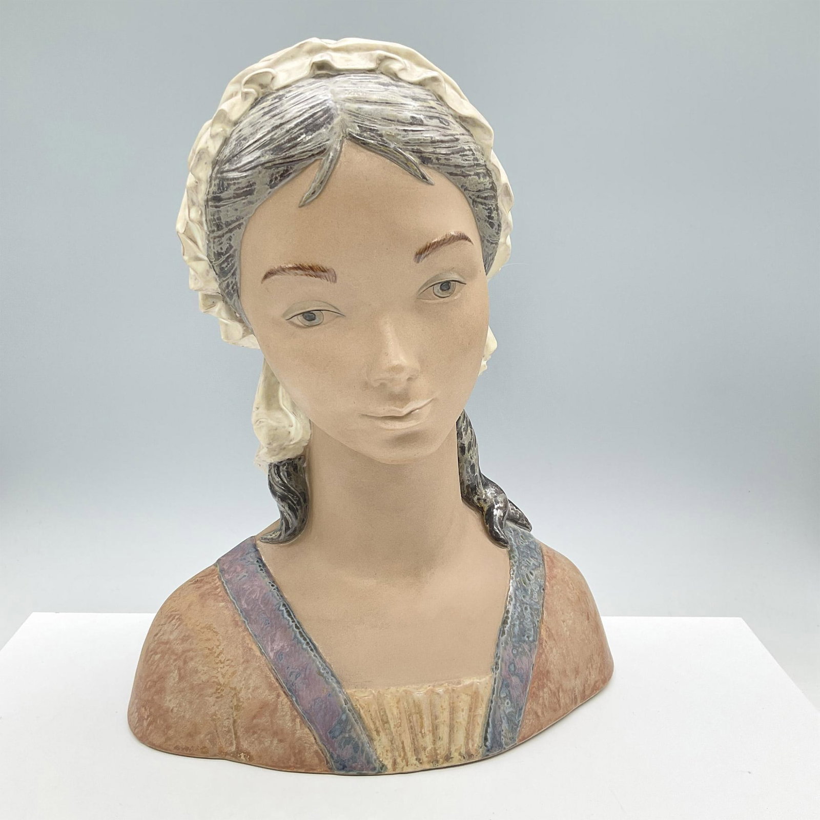 Little Girl - Lladro Porcelain Bust: Gres finish. Depicts a girl with a sweet calm gaze. Lladro backstamp. Artist: Fulgencio Garcia Issued: 1971 - 1985 Dimensions: 10.5''L x 5.5''W x 13.5''H Manufacturer: Lladro Country of Origin: S