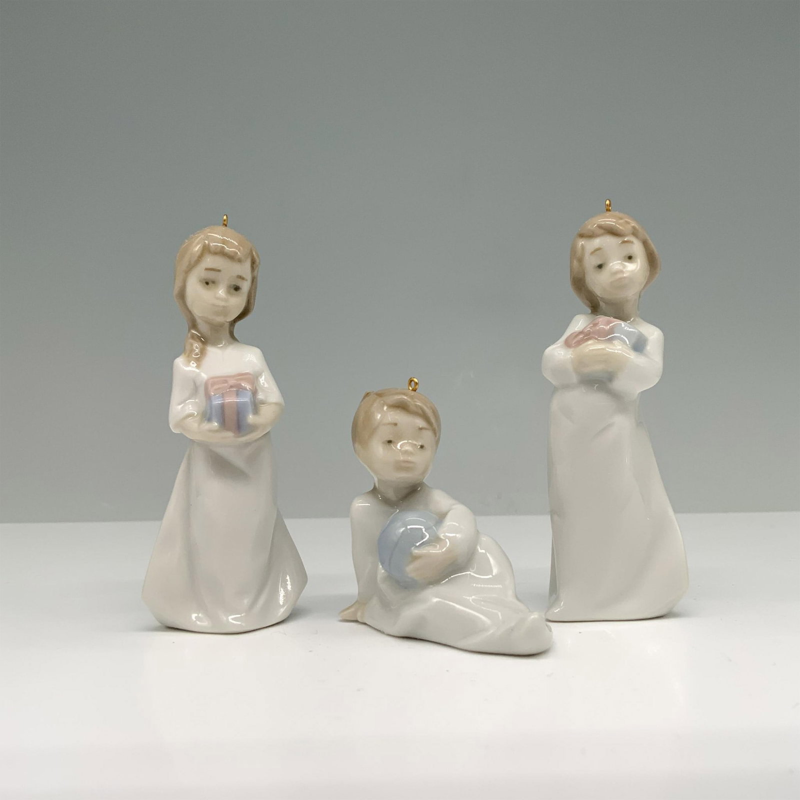 Lladro Porcelain Tree Ornament Set Christmas Morning 1005940: Glossy finish. This set includes three children in white robes holding gifts. Lladro backstamps. The largest ornament measures 1.25"L x 1"W x 3.5"H. Artist: Joan Coderch Issued: 1992-1992 Dimensions: 