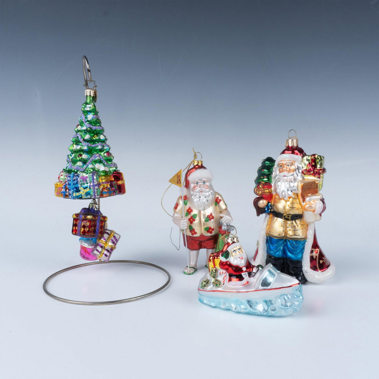 4pc Radko and Radko Style Ornaments: This grouping includes a Radko Christmas tree with three hanging ornaments, a Christmas Eve Santa from Marquis by Waterford, an unmarked Golfing Santa, and an unmarked Santa in a boat. The largest pie