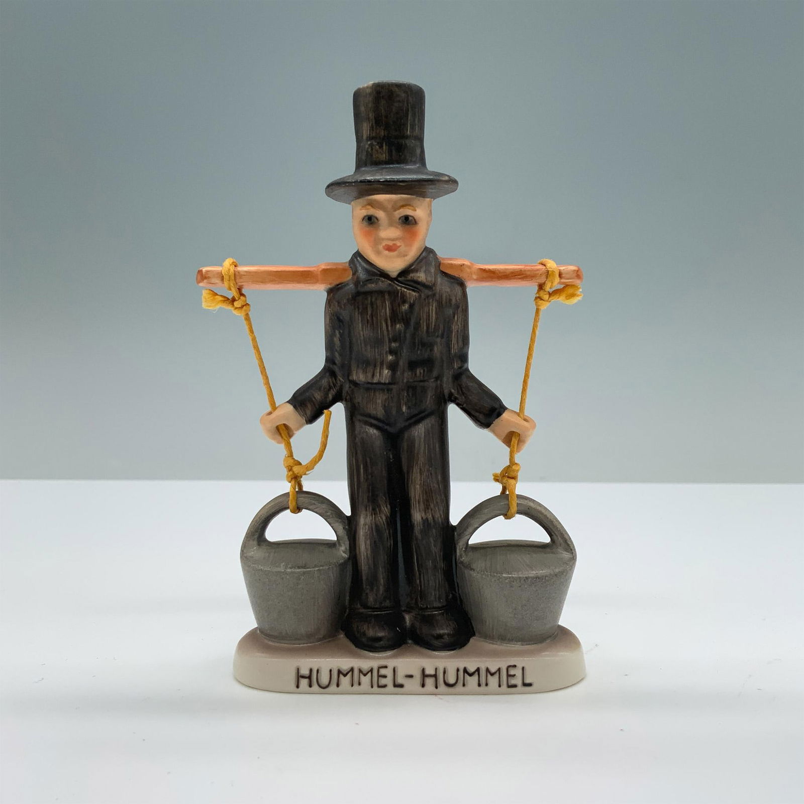Goebel Hummel Figurine, Mors Water Carrier: Hand-painted porcelain with matte finish features a mors carrying two water buckets. Goebel backstamp. Hummel-Hummel impressed on the base. Dimensions: 3"L x 1"W x 4.5"H Manufacturer: Goebel Hummel Co