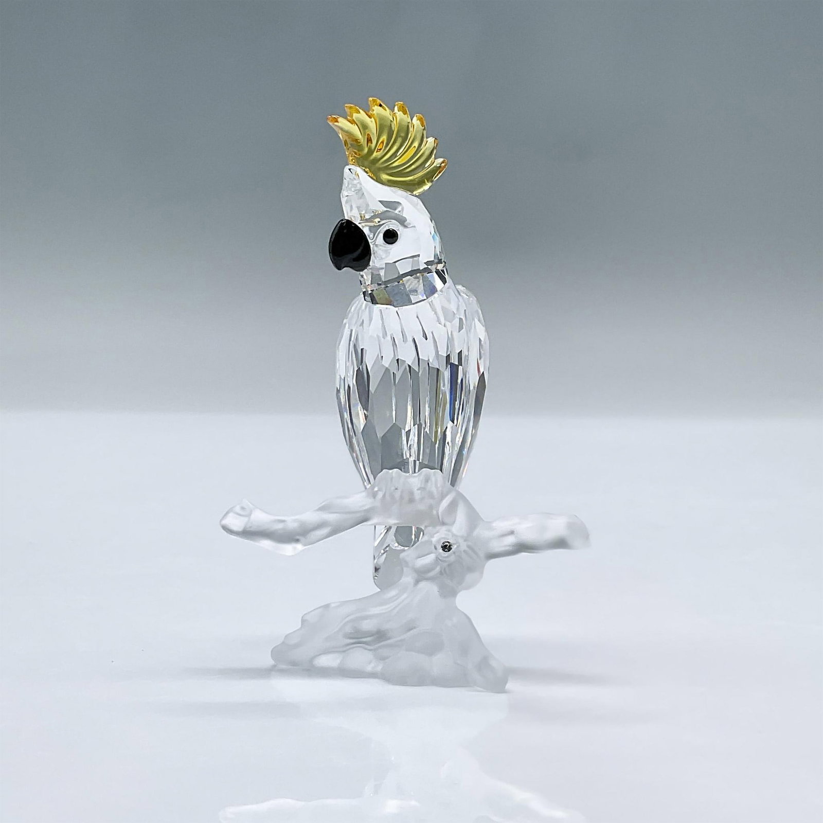Swarovski Crystal Figurine, Cockatoo: This charming bird features a clear crystal facetted body, a black beak and yellow crest. This item has its original box measuring 3.25"L x 3.25"W x 6.25"H. Swarovski acid mark. 261635. Artist: Heinz 